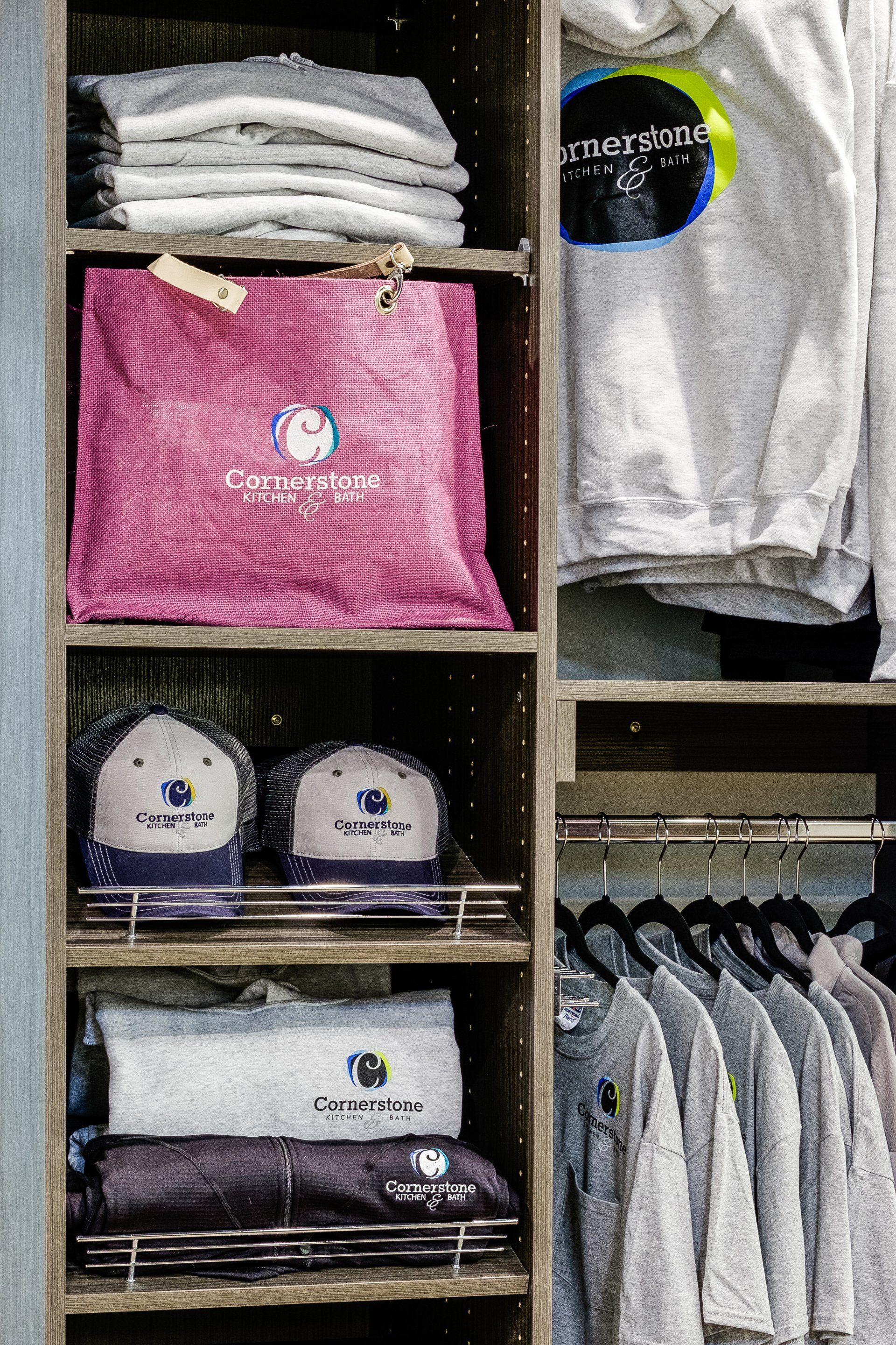 Folded shirts and sweatshirts displayed on store shelves and hanging racks, including a pink item and gray hoodie.