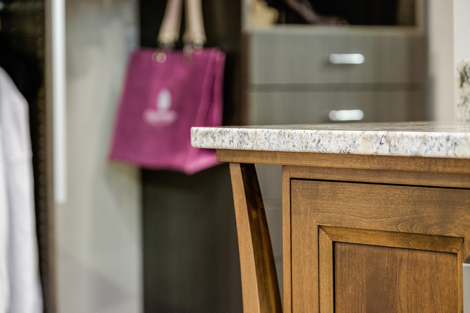 Kitchen counter with wooden cabinet, granite top, and a pink bag in the background