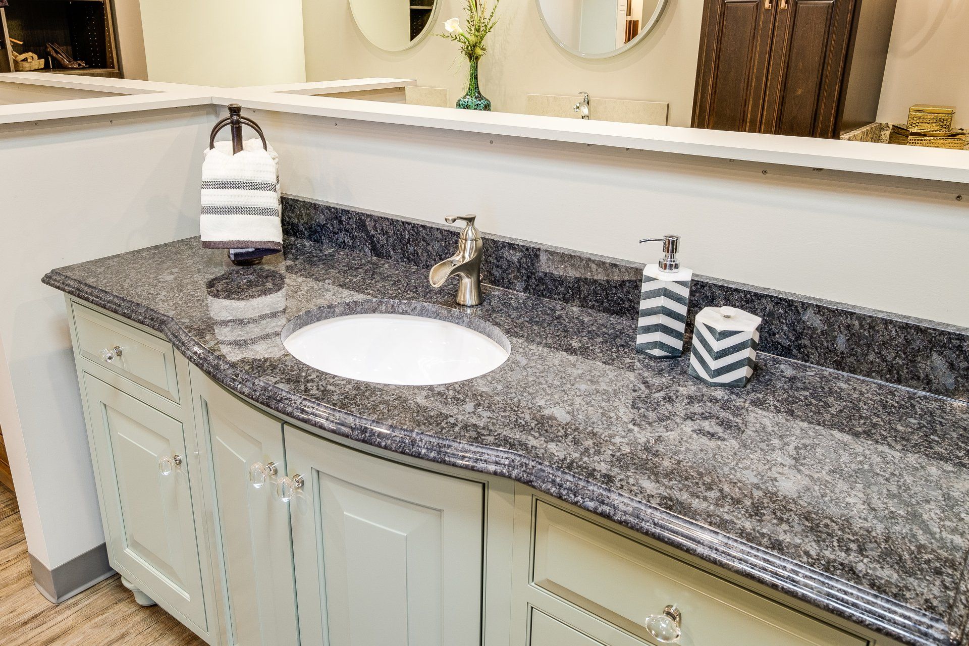 White bathroom vanity with speckled granite countertop, oval sink, and decorative soap dispensers by a mirror