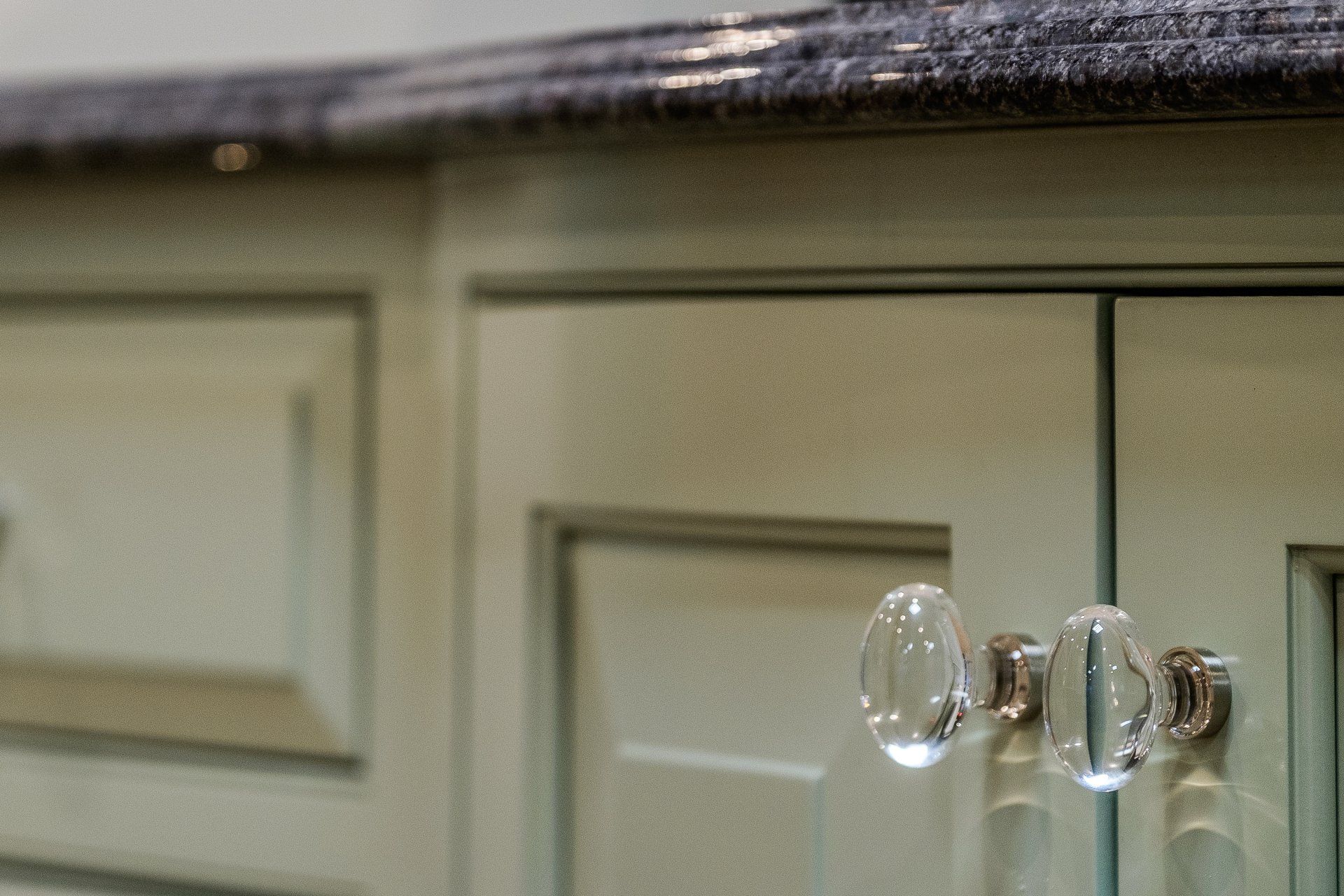 Clear glass cabinet knobs on a cream kitchen cabinet door, close-up.