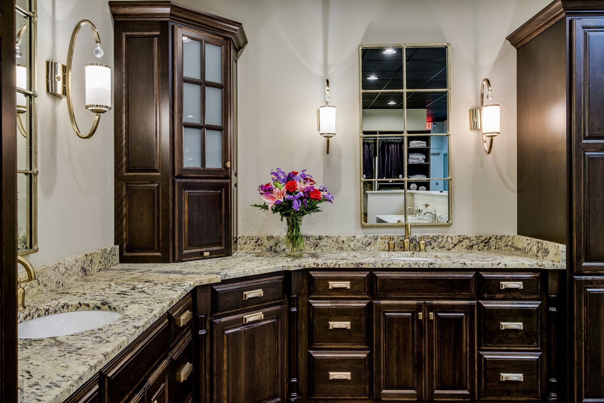 Elegant bathroom vanity with dark wood cabinets, speckled granite countertop, and a vase of flowers beneath wall lights