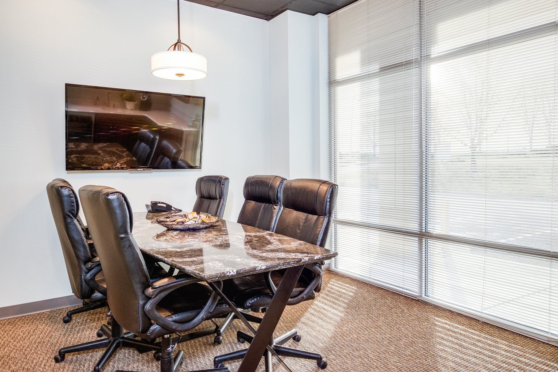 Modern conference room with black chairs, glass table, wall art, and large window blinds