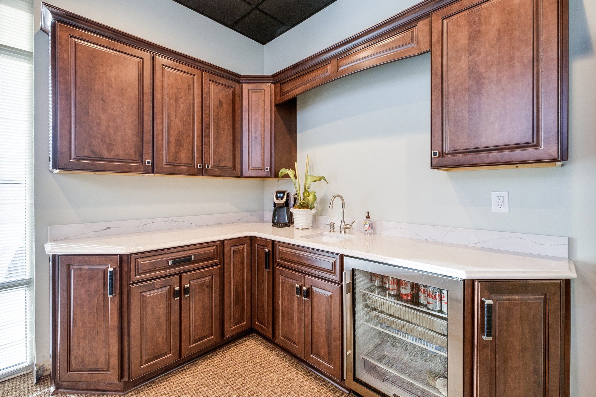 Empty kitchen corner with dark wood cabinets, light countertops, and stainless wine fridge.