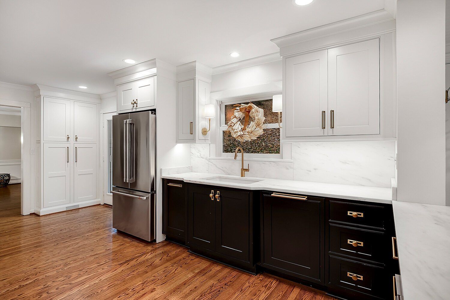 Bright modern kitchen with stainless steel fridge, white cabinets, dark lower cabinets, and hardwood floors.