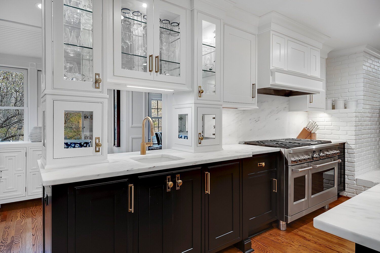 Bright modern kitchen with white cabinets, black island, stainless stove, and hardwood floors