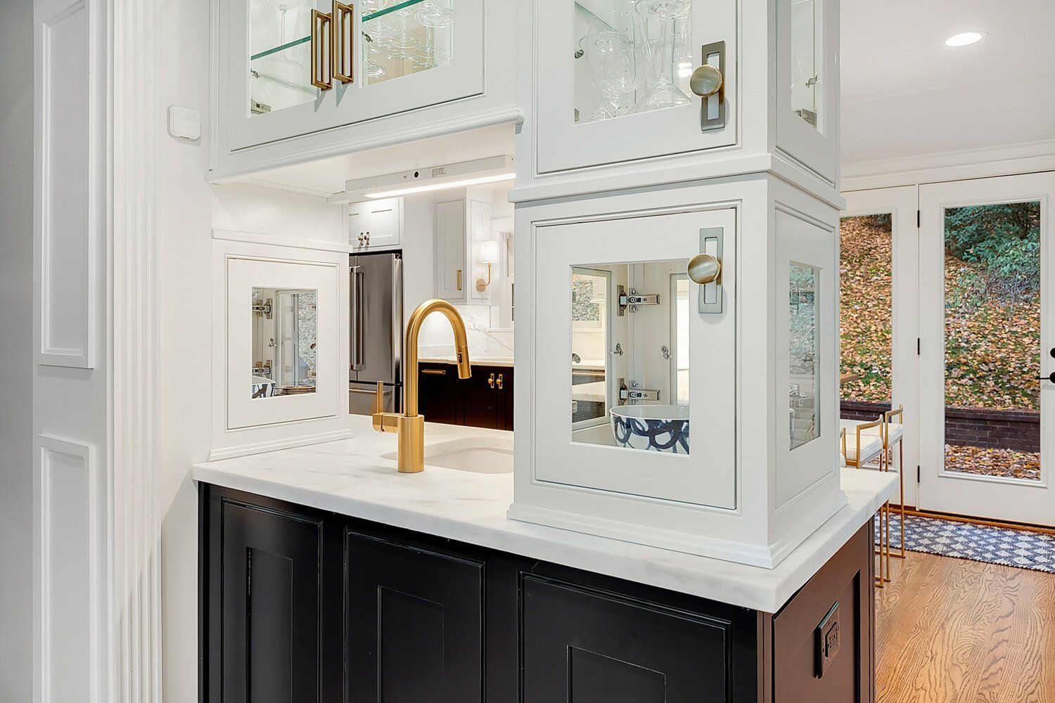 Modern vanity area with white mirrored cabinets, gold faucet, and black base cabinetry in a bright room
