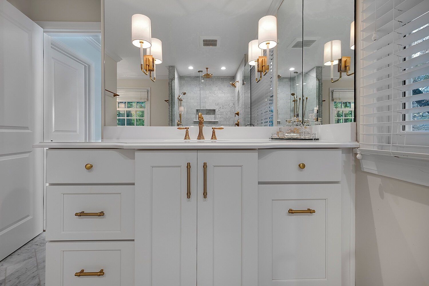 Bright white bathroom vanity with gold hardware, twin sinks, mirrors, and sconces.