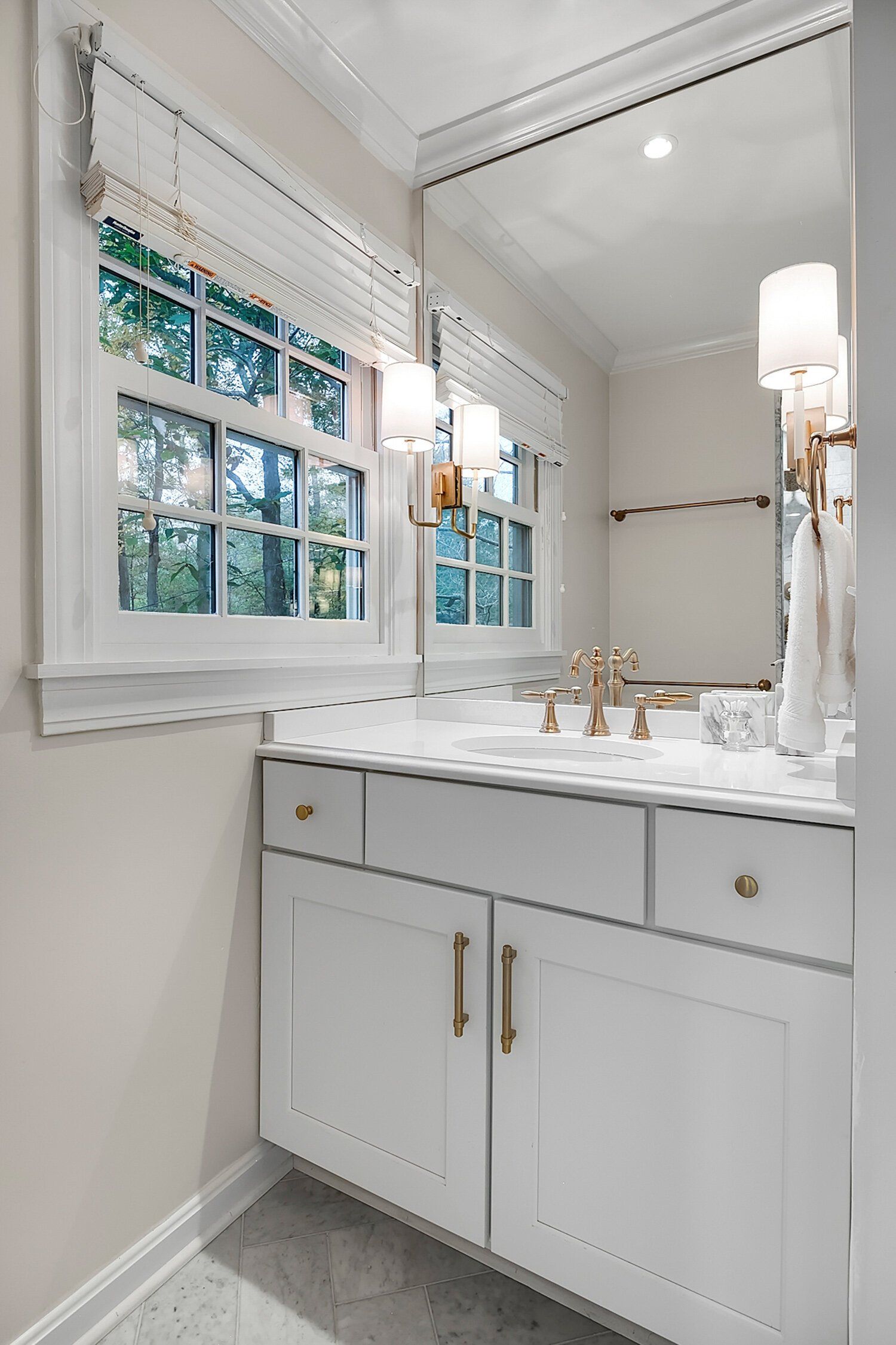 Bright white bathroom vanity with mirror, brass hardware, and a window beside it