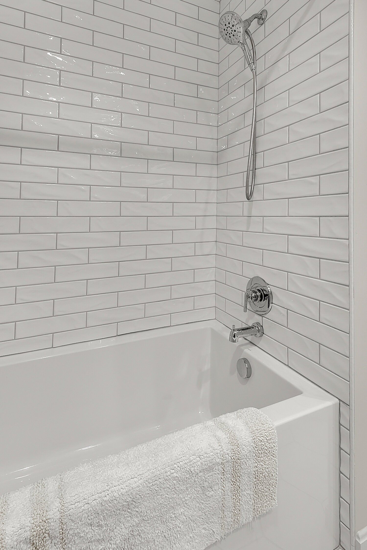 Small bathroom with white tile walls and a bathtub with a white towel draped over the side.
