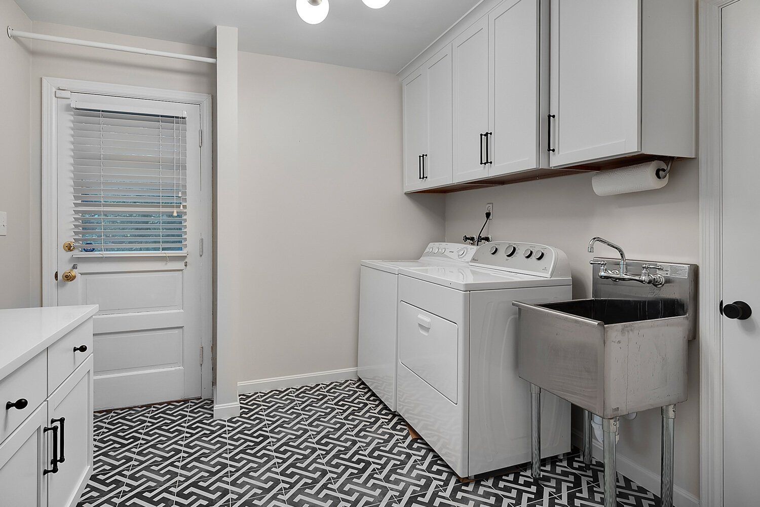 White laundry room with washer, sink, cabinets, and patterned black-and-white floor