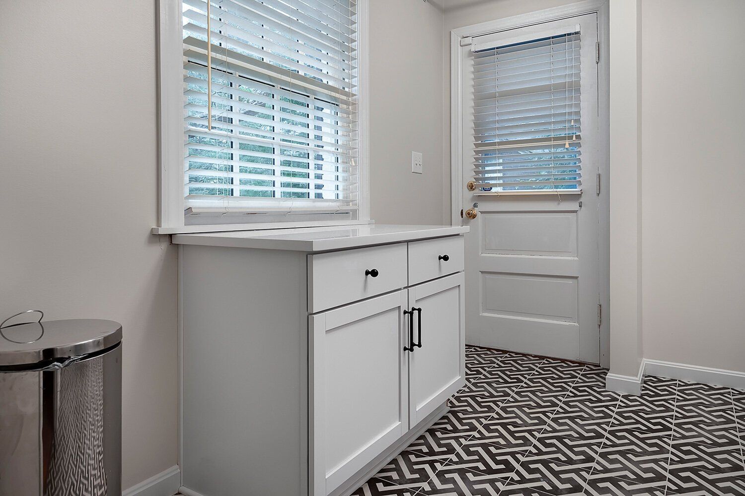 Small bright entryway with white cabinets, windows, a door, and patterned tile flooring.