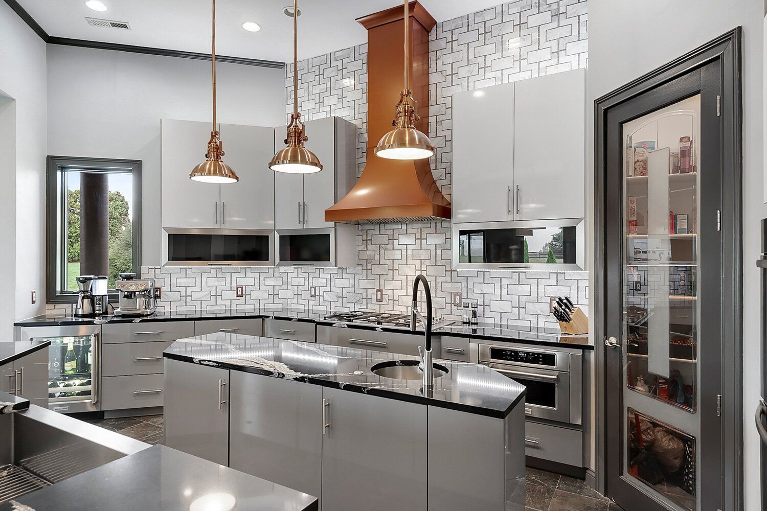 Modern kitchen with gray cabinets, copper pendant lights, marble island, and glass wine cooler