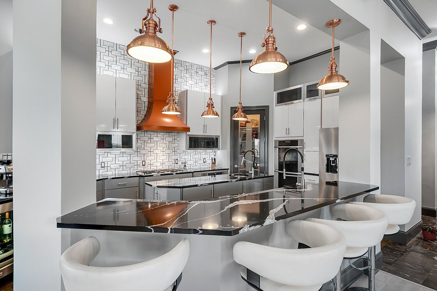 Modern white kitchen with copper pendant lights, black island, and white barstools