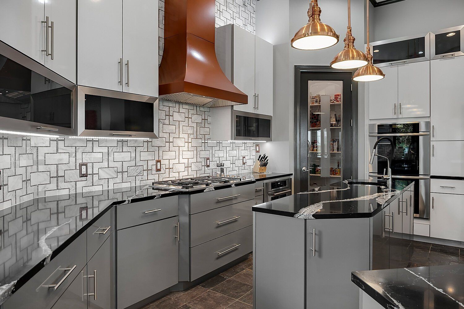 Modern kitchen with gray cabinets, black countertops, mosaic backsplash, and copper pendant lights