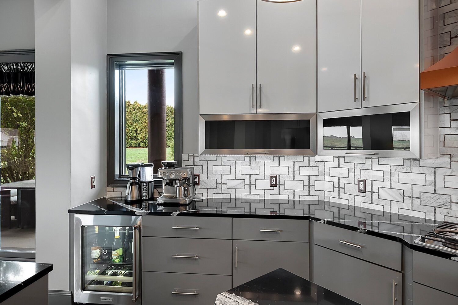 Modern kitchen with gray cabinets, mosaic backsplash, black countertops, and stainless steel appliances