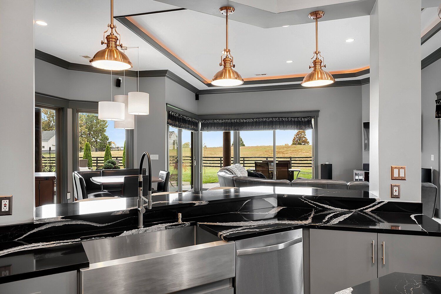 Modern kitchen with black countertops, copper pendant lights, and an open view to a patio and water.