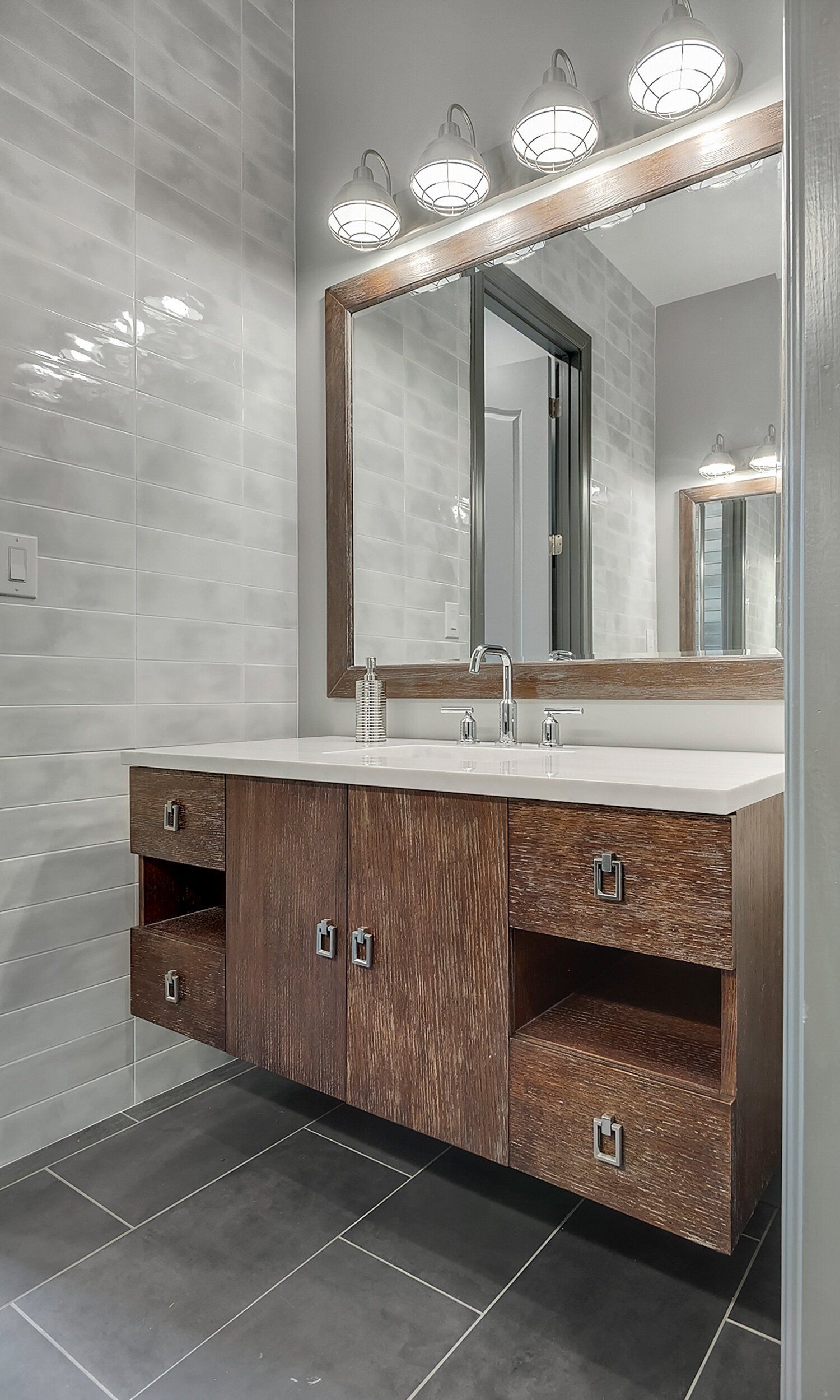Modern bathroom vanity with wood cabinets, white countertop, large mirror, and wall sconces.