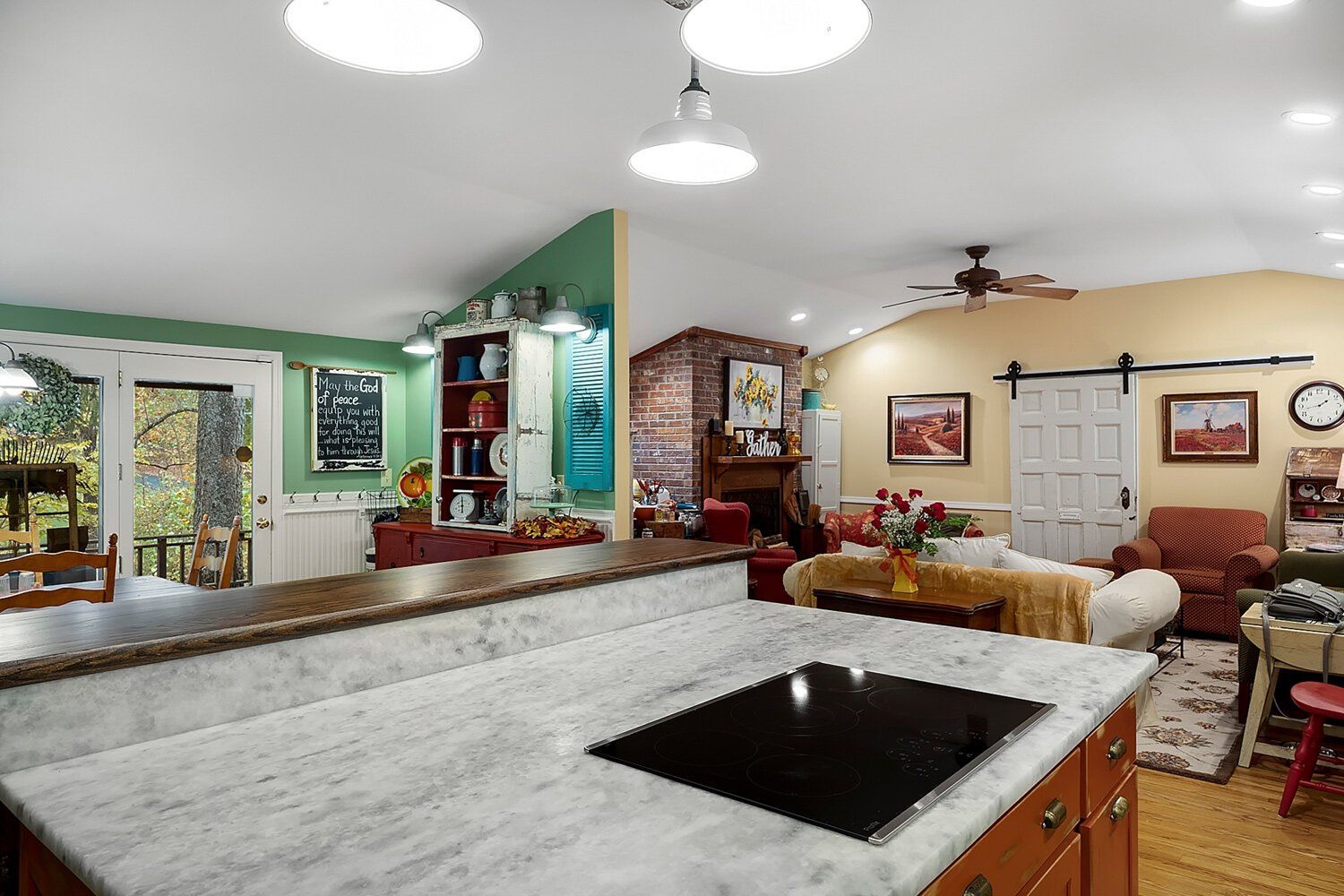 Open kitchen and living room with marble island, green accent wall, and beige sofa.