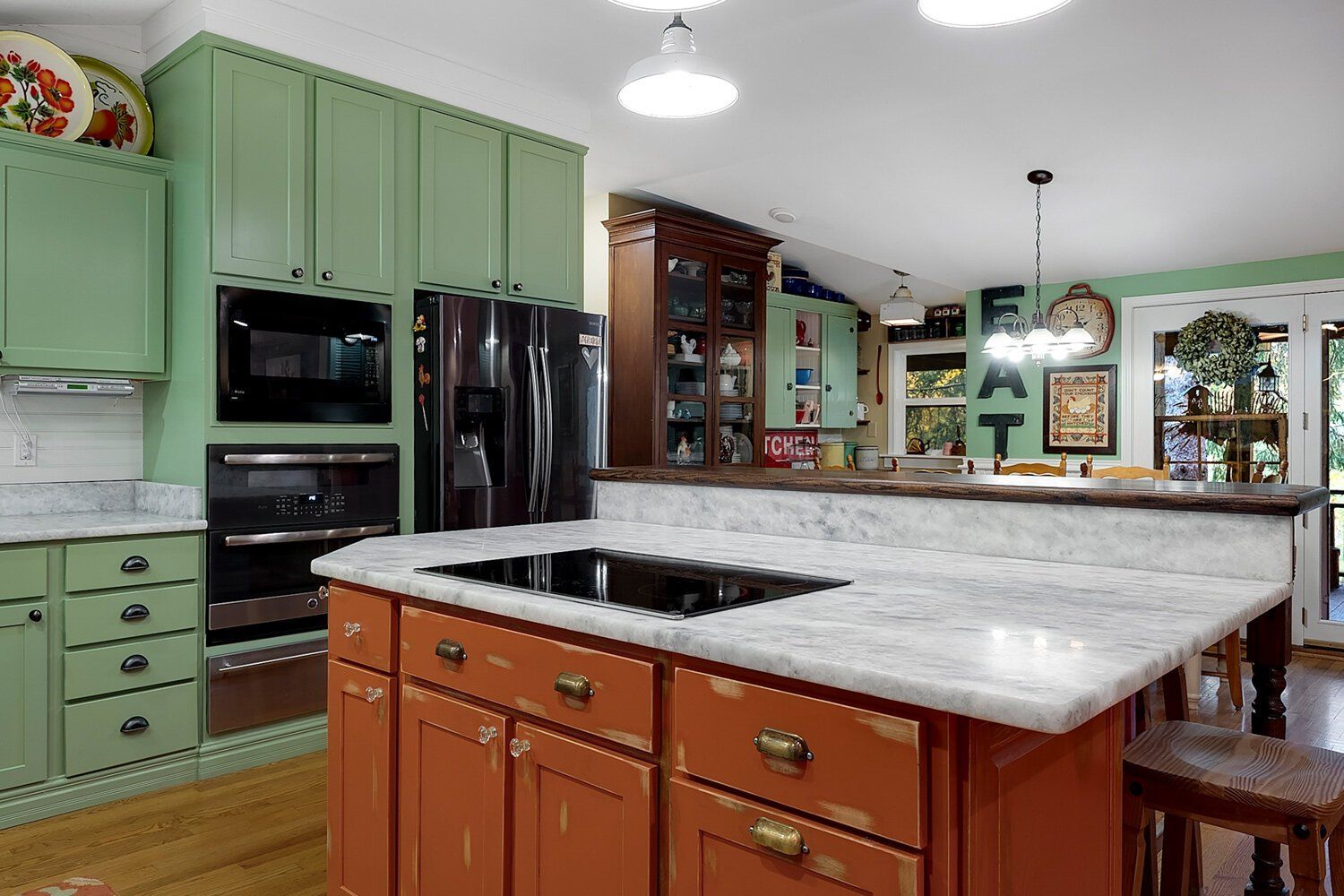 Spacious kitchen with green cabinets, black appliances, and a marble-topped island in the foreground
