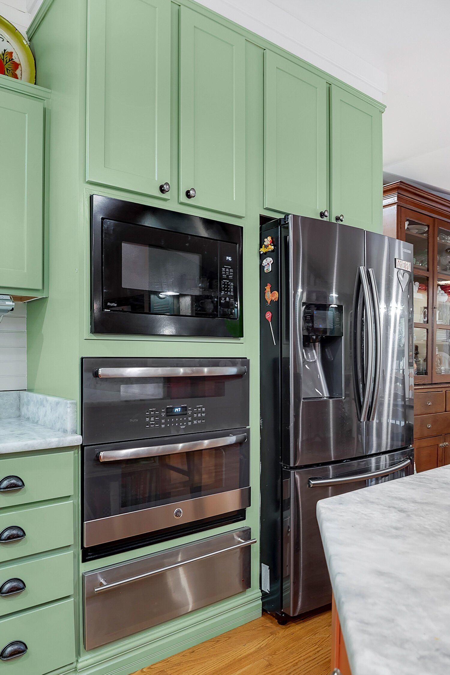 Mint-green kitchen cabinets with built-in ovens and a stainless steel refrigerator.