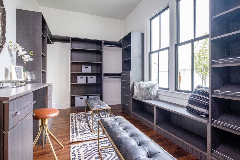Modern home office with built-in shelves, dark wood floor, large windows, and a bench by the window