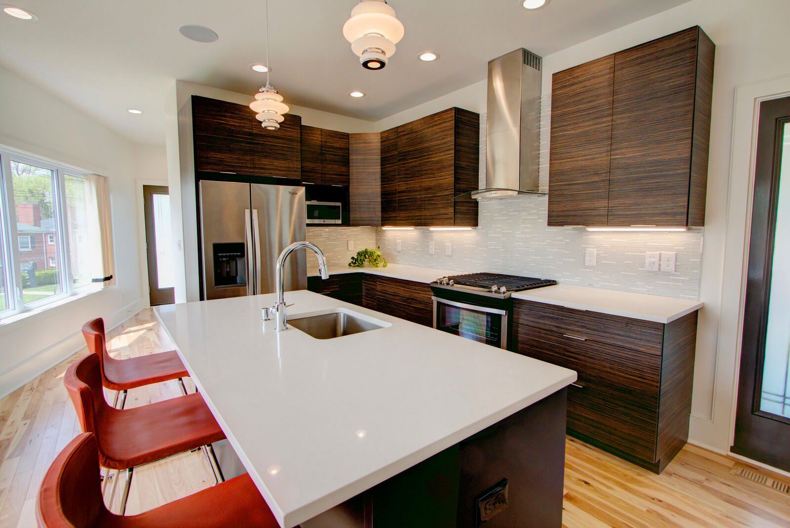 Modern kitchen with white island, red stools, stainless appliances, and dark wood cabinets