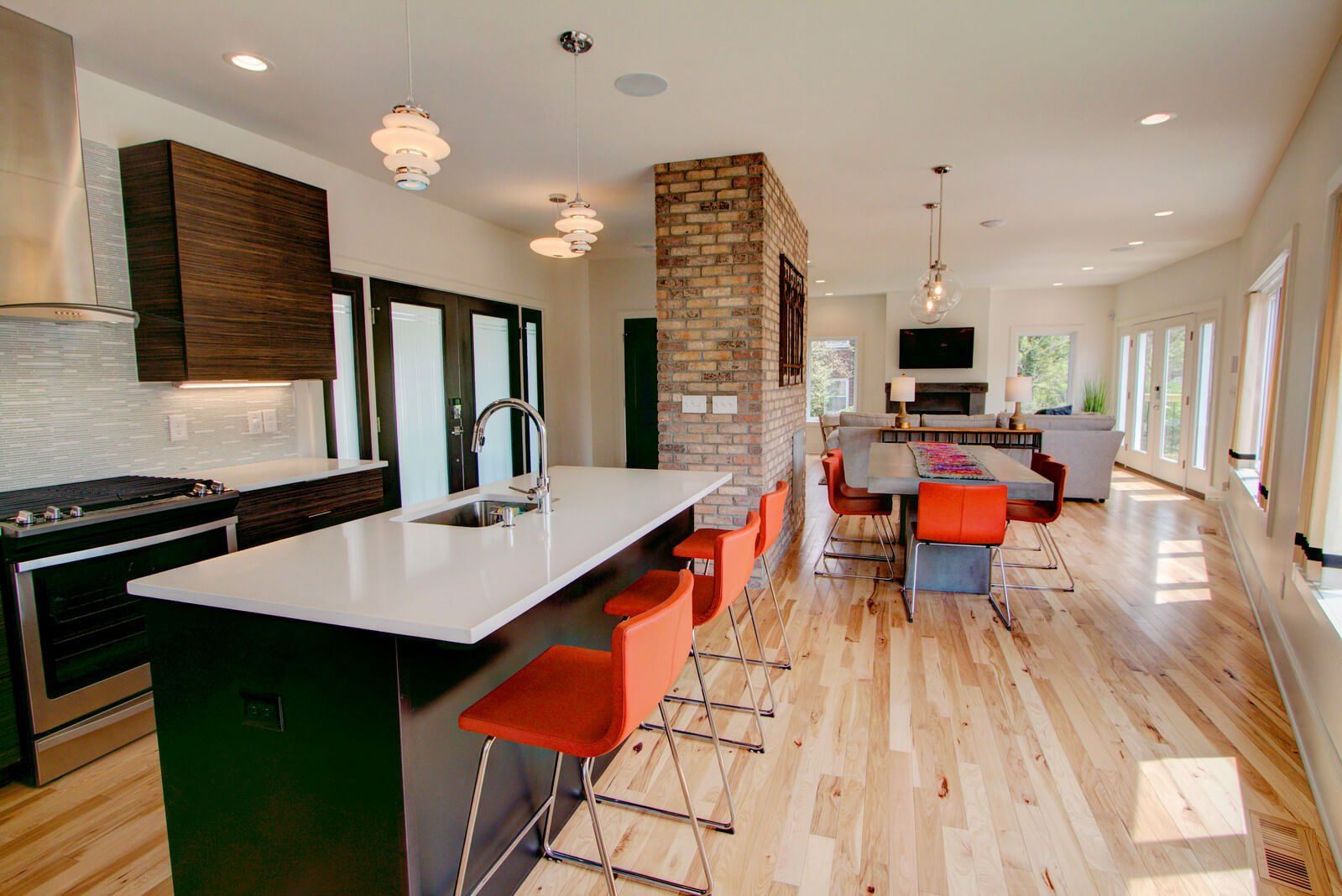 Modern open-plan kitchen and dining room with brick accents, black island, orange stools, and hardwood floors