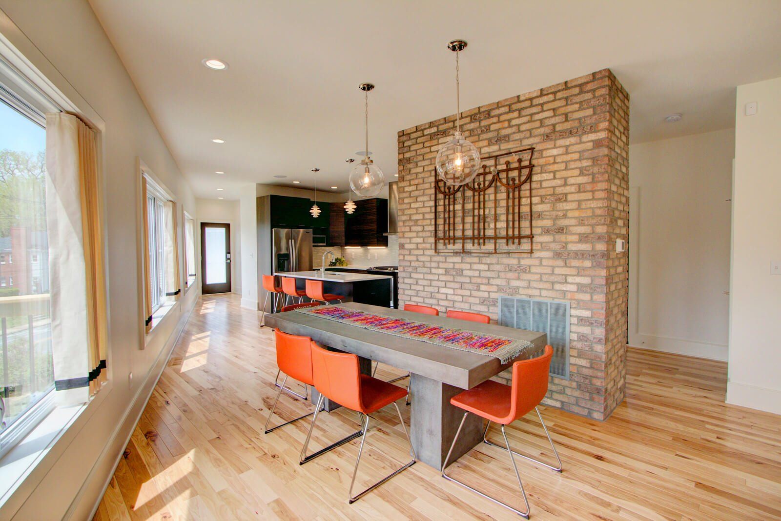 Bright dining room with brick accent wall, wooden table, orange chairs, and open kitchen.