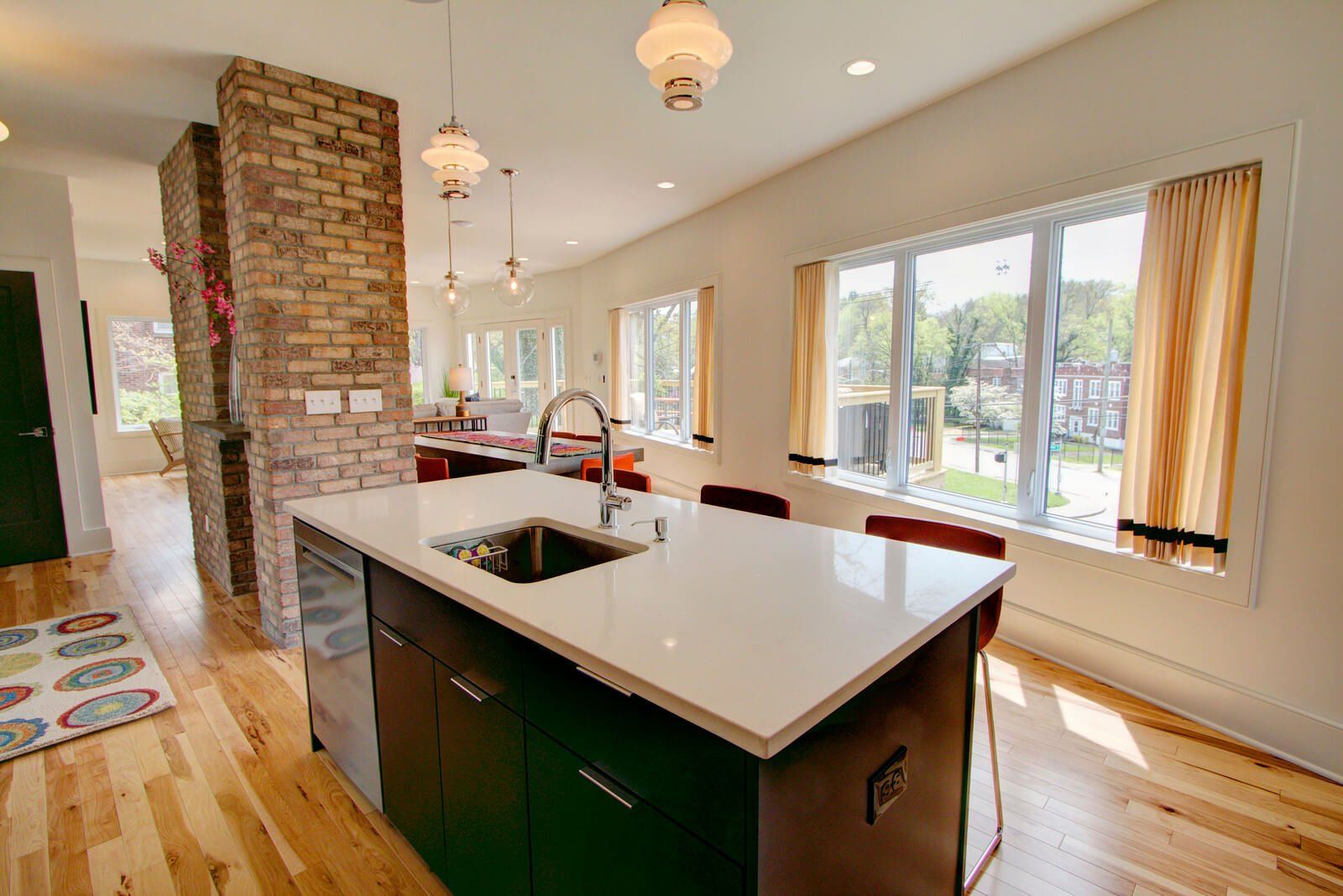 Bright kitchen with island, brick chimney, hardwood floors, and large windows overlooking a garden