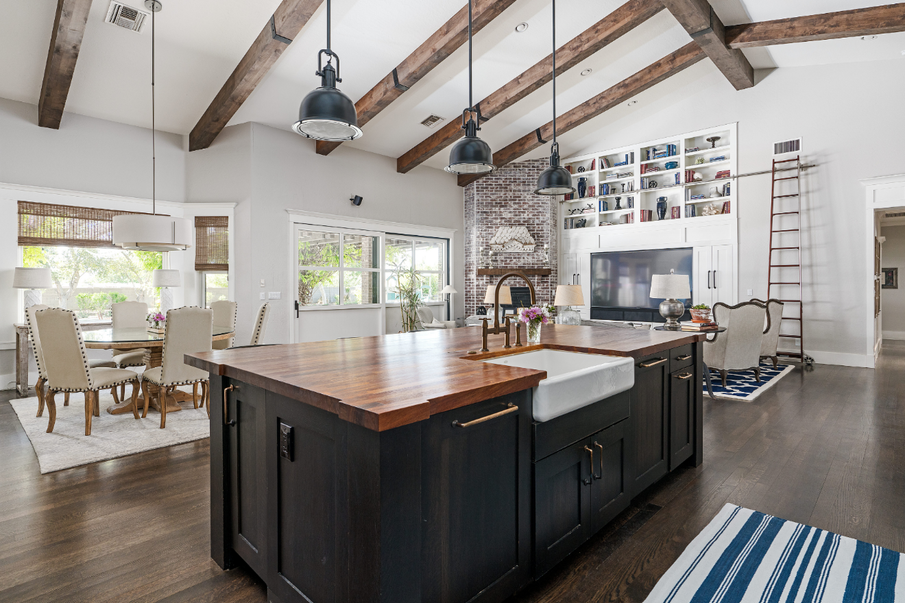 Modern open-plan kitchen and dining room with dark island, wood beams, and large windows