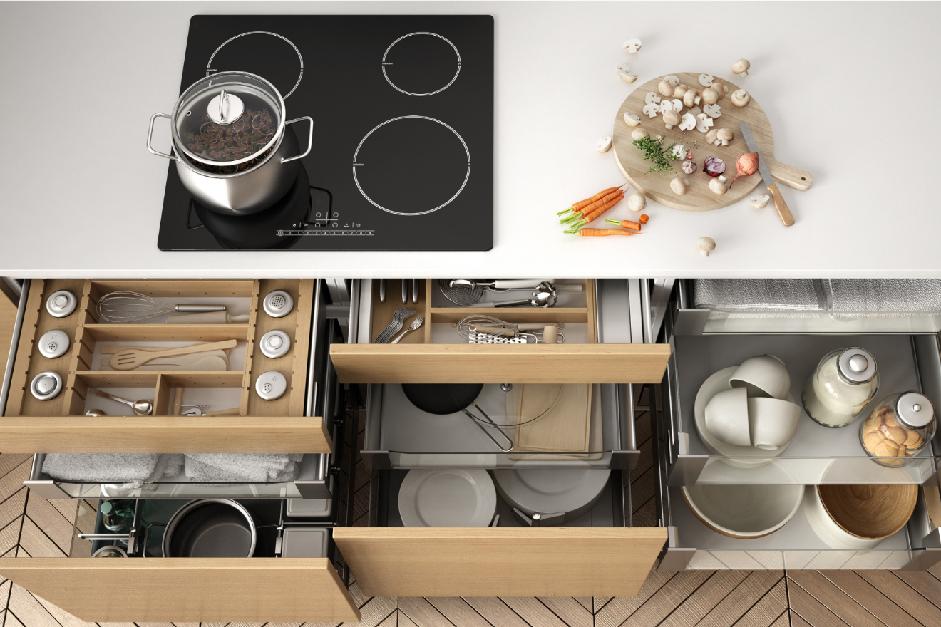 Top-down view of a kitchen with stovetop, cutting board, and open drawers holding utensils and dishes