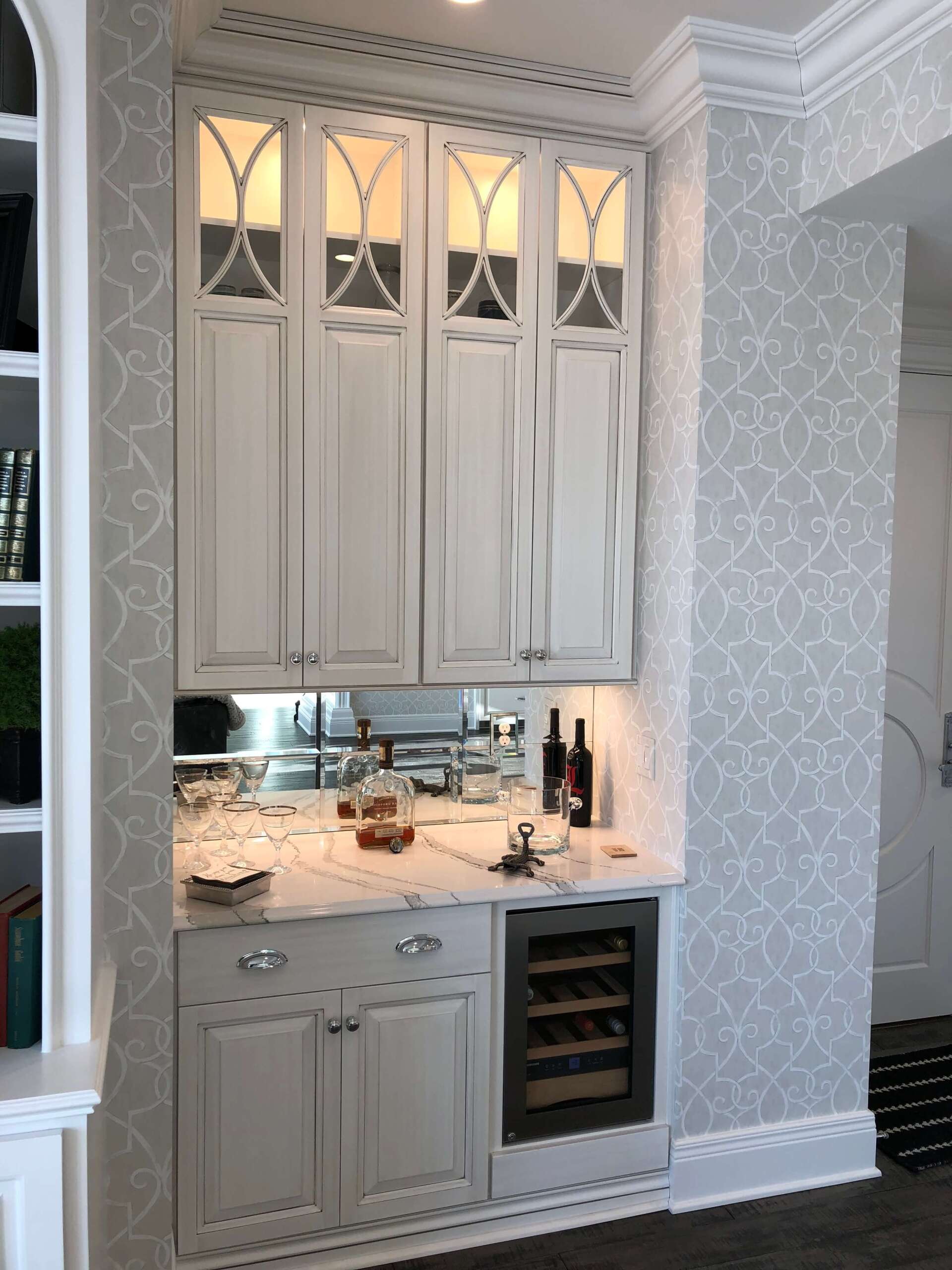 Built-in white kitchen bar cabinet with under-cabinet lighting, glass-front uppers, and wine rack.
