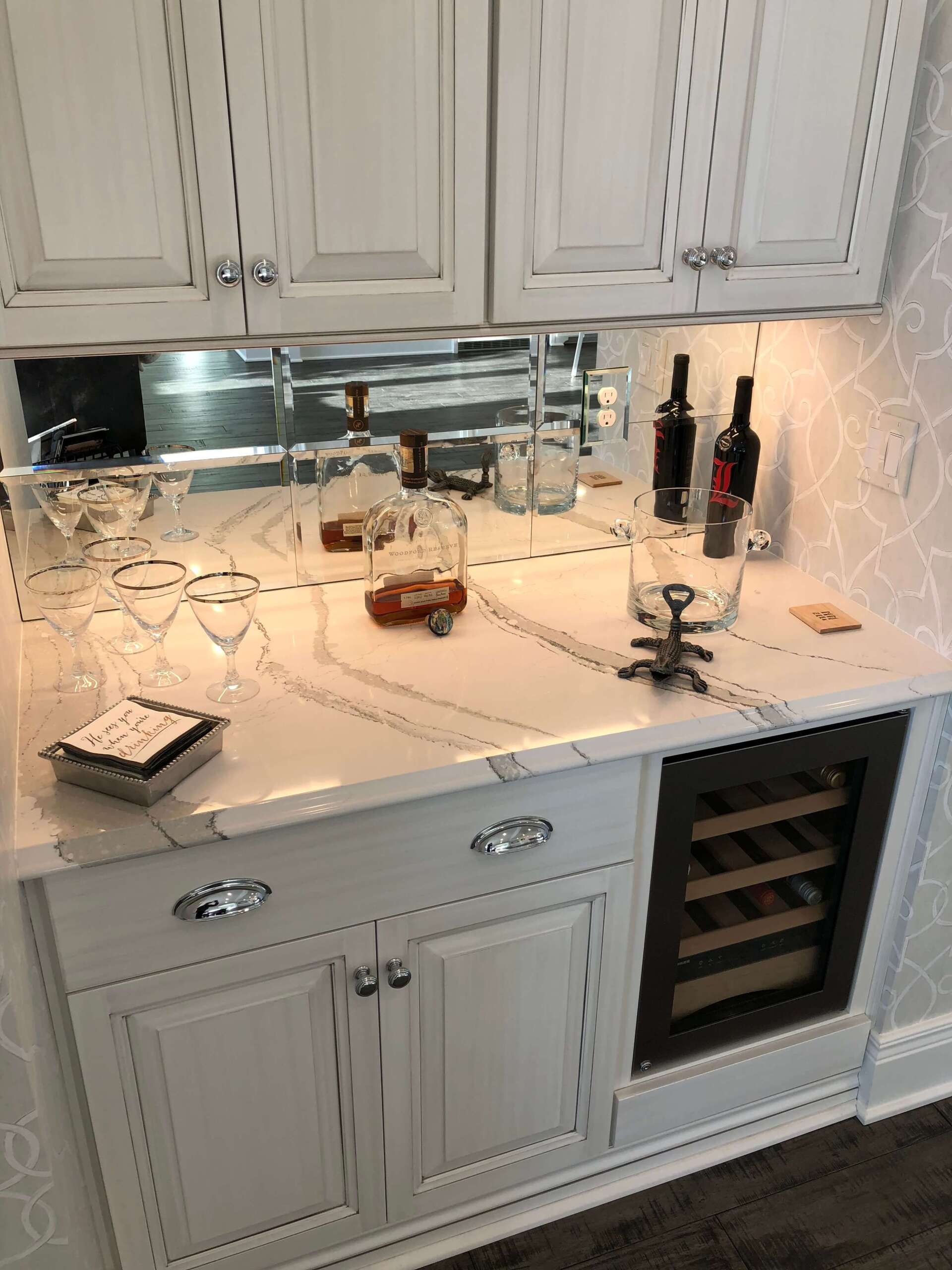 White kitchen countertop with sink, candles, wine bottles, and an under-counter wine rack