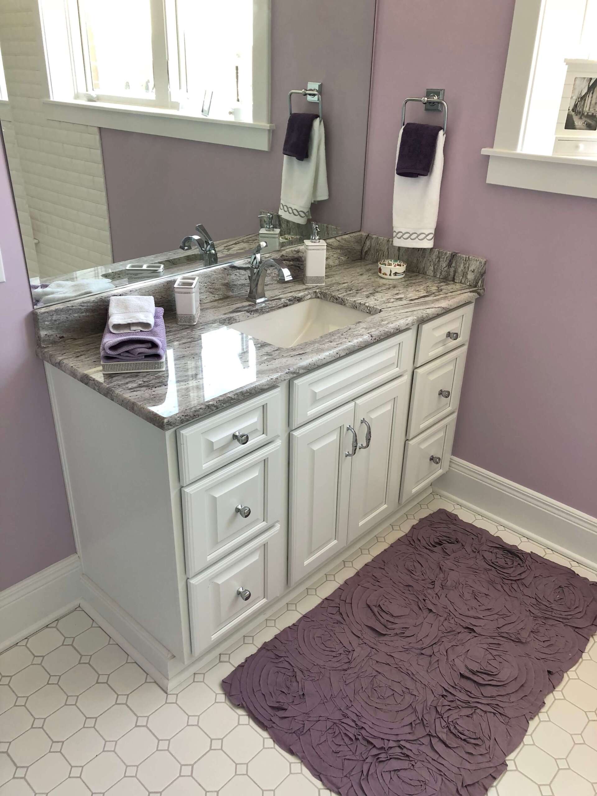 White vanity with granite top, sink, mirror, and purple accents in a bathroom.