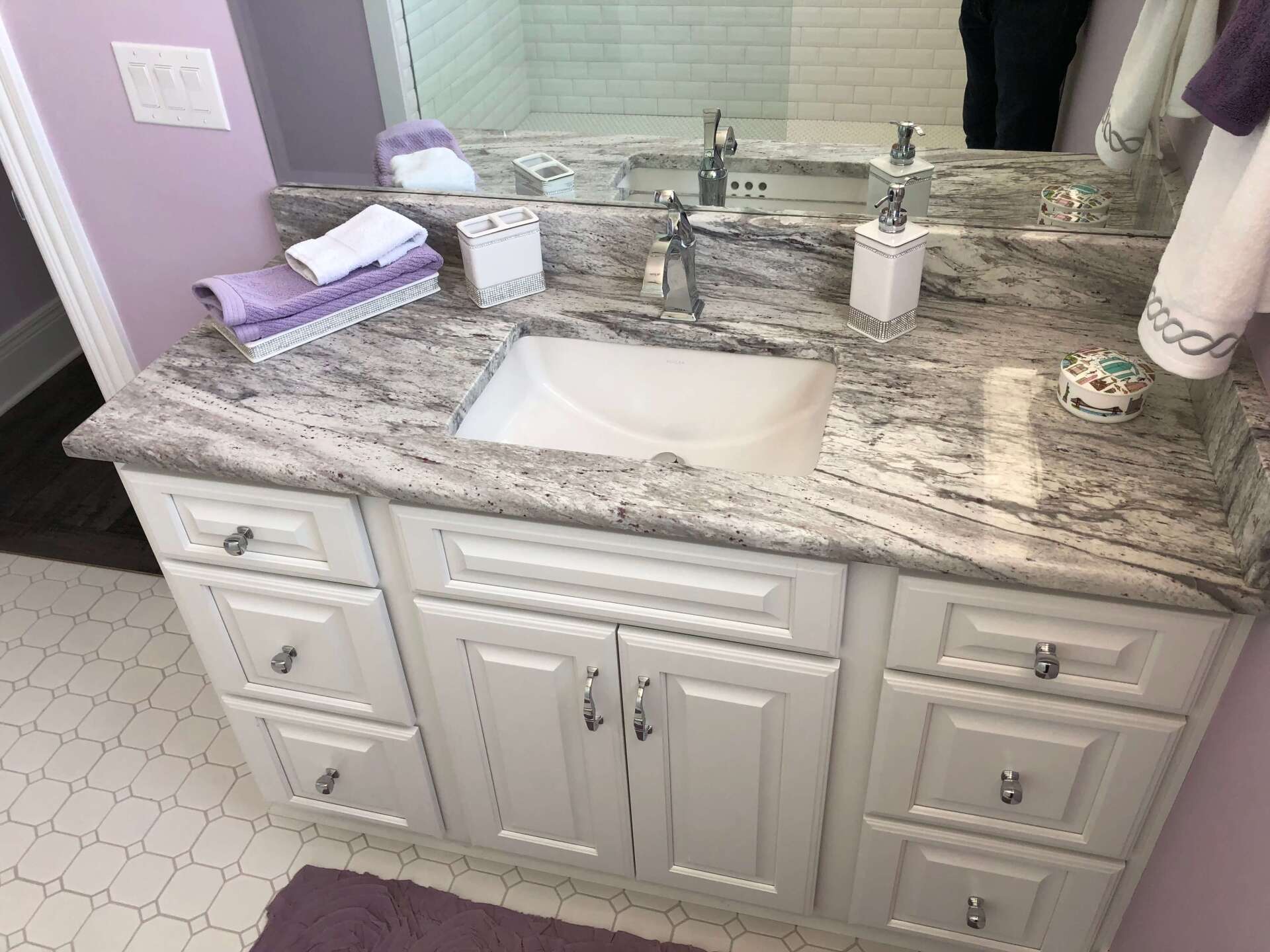 White bathroom vanity with speckled granite countertop, dual sinks, and a large mirror.