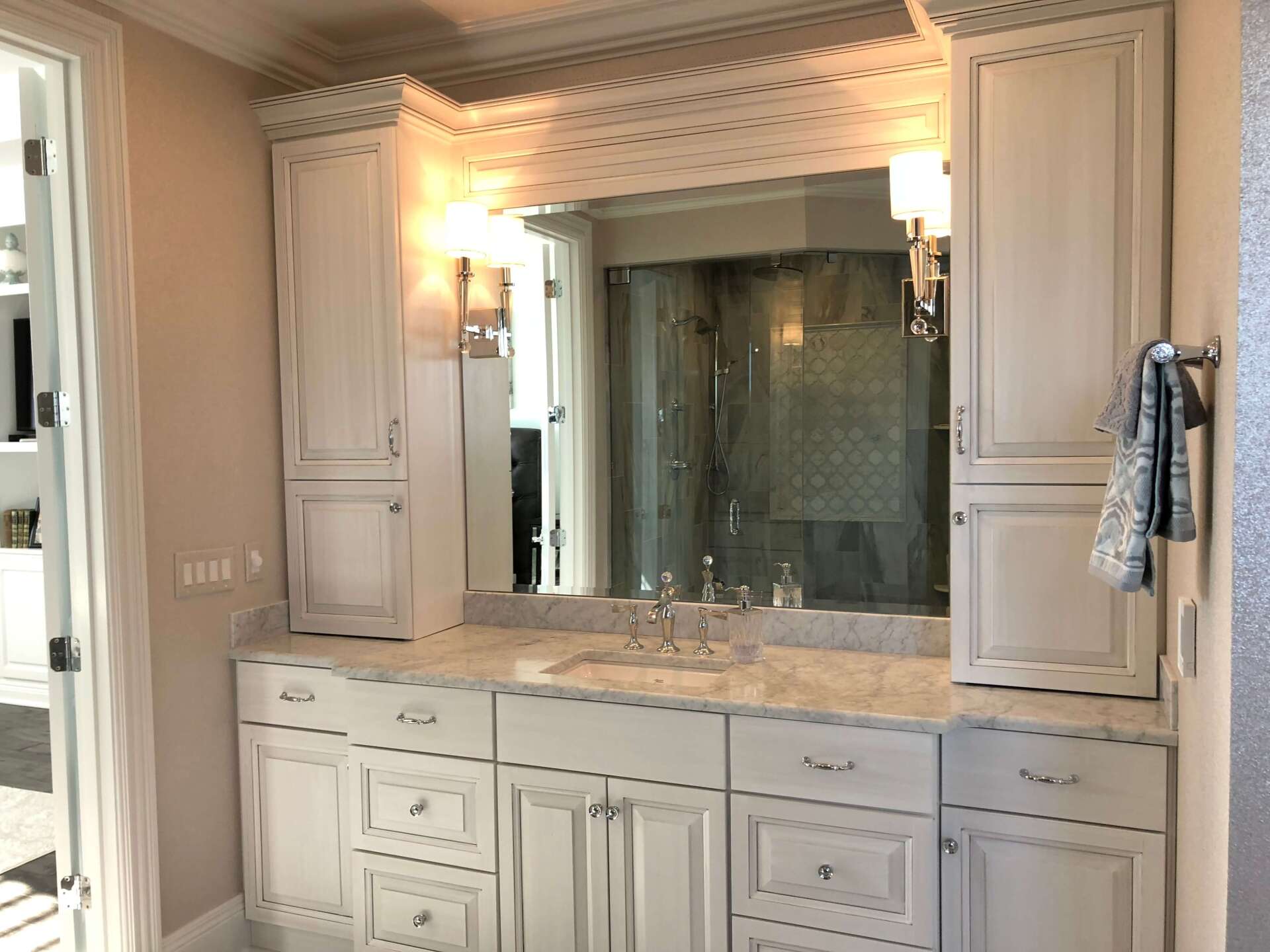 Elegant bathroom vanity with mirror, marble countertop, and wall sconces in a cream-colored interior