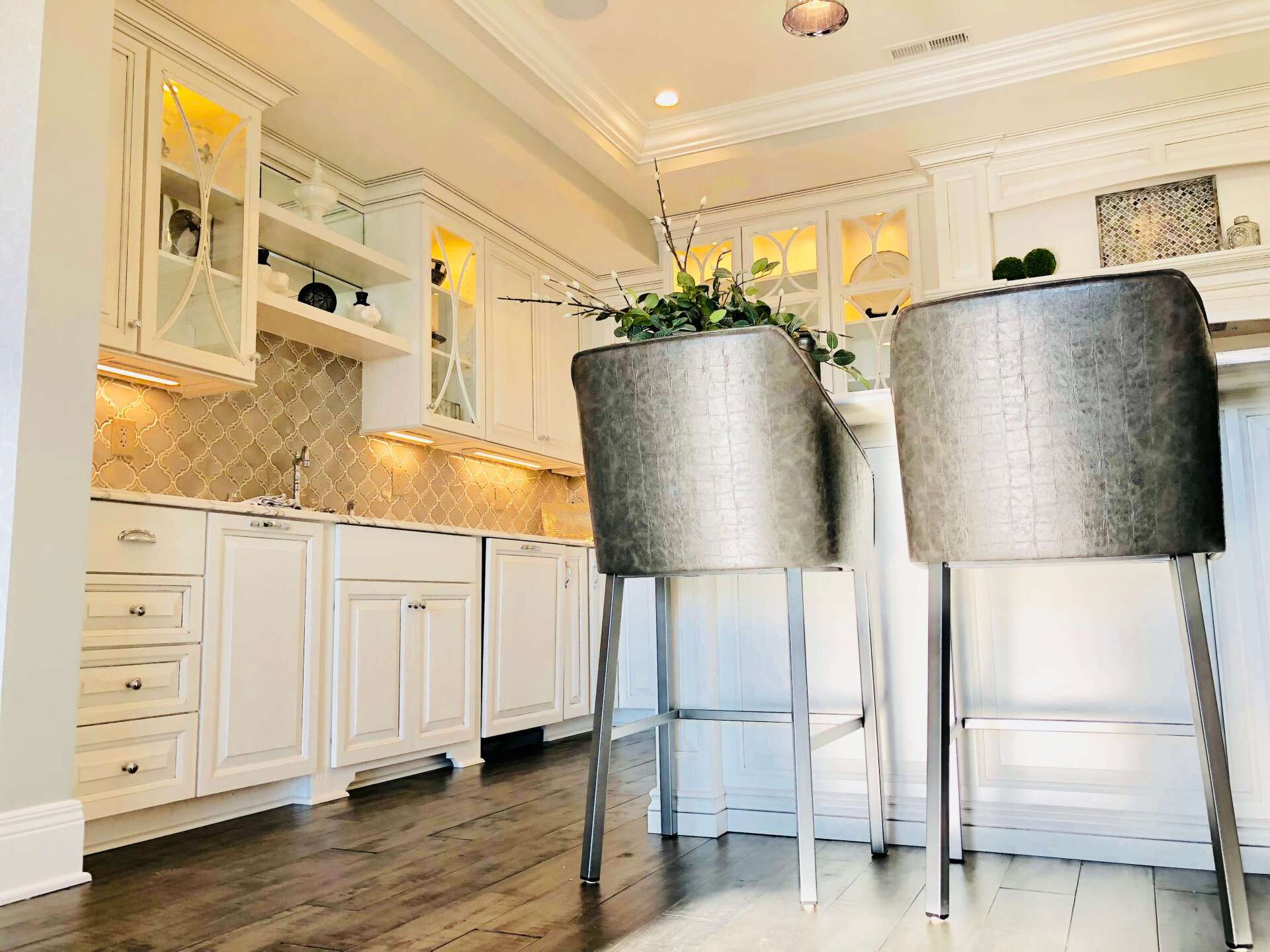 Bright white kitchen with marble island, gray bar stools, and dark wood floor