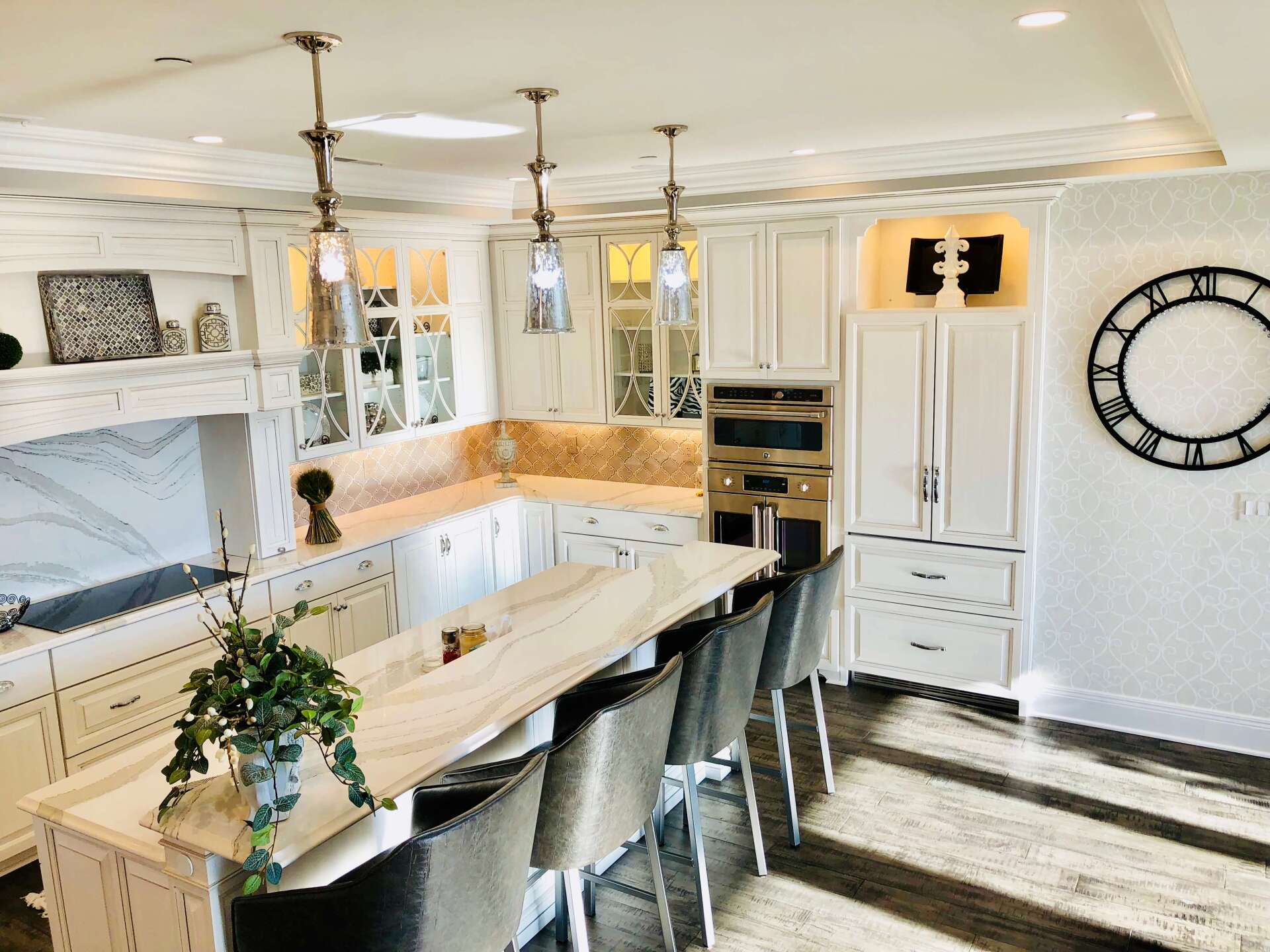Bright white kitchen with island, pendant lights, built-in fridge, and large wall clock