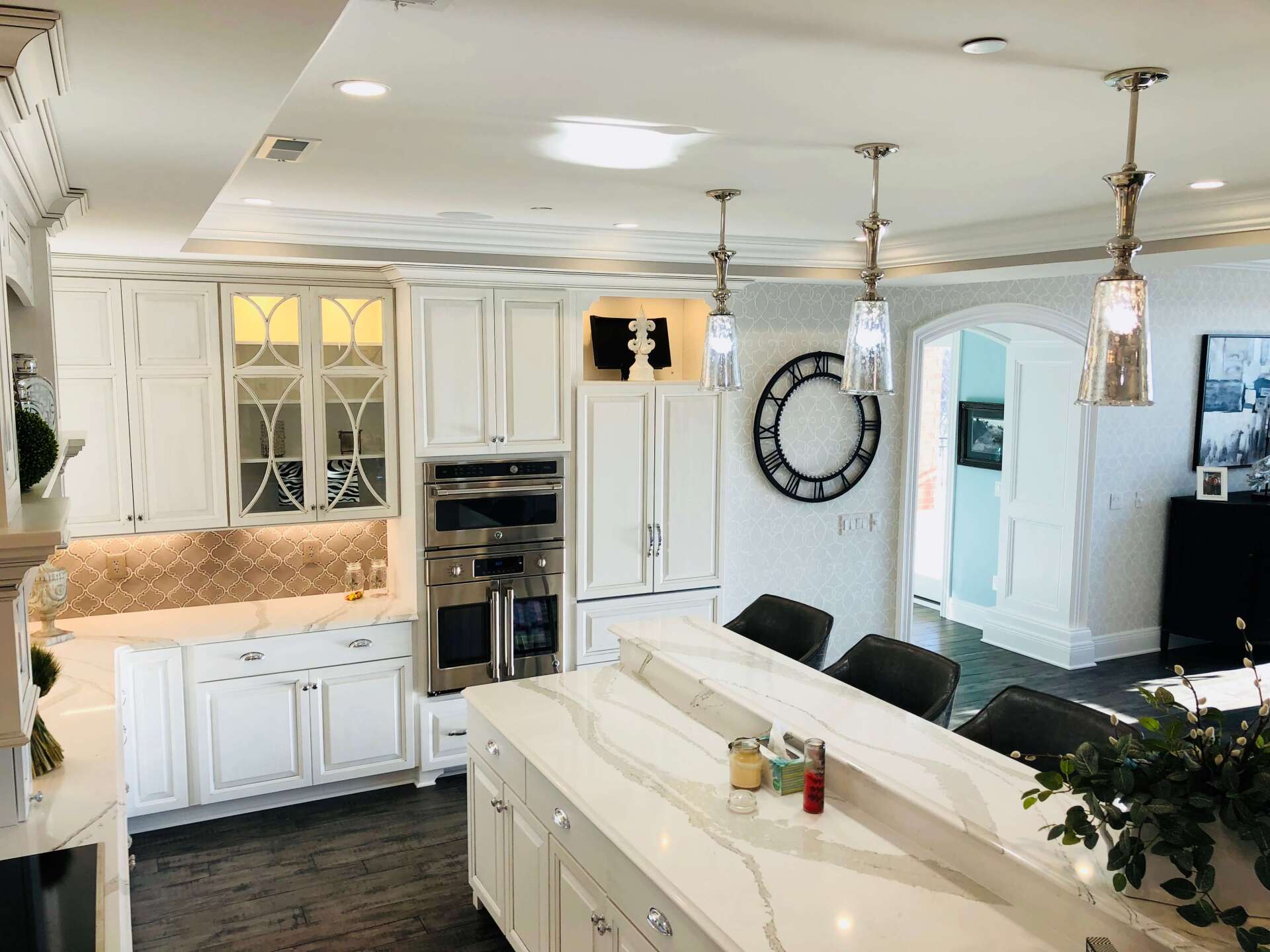 Bright white kitchen with island, cabinets, pendant lights, and a large wall clock