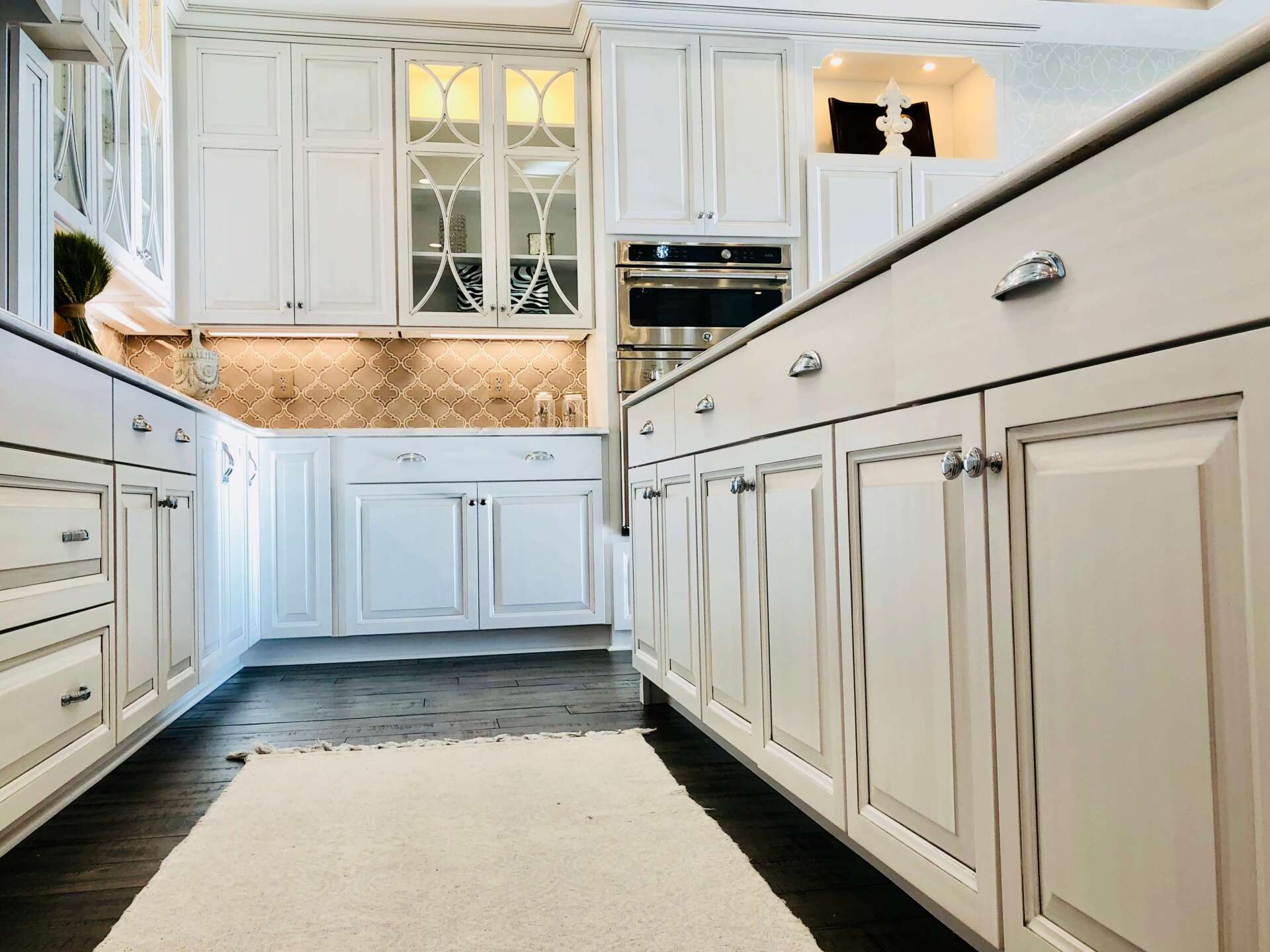 Bright white kitchen with marble island, paneled cabinets, and dark hardwood floor