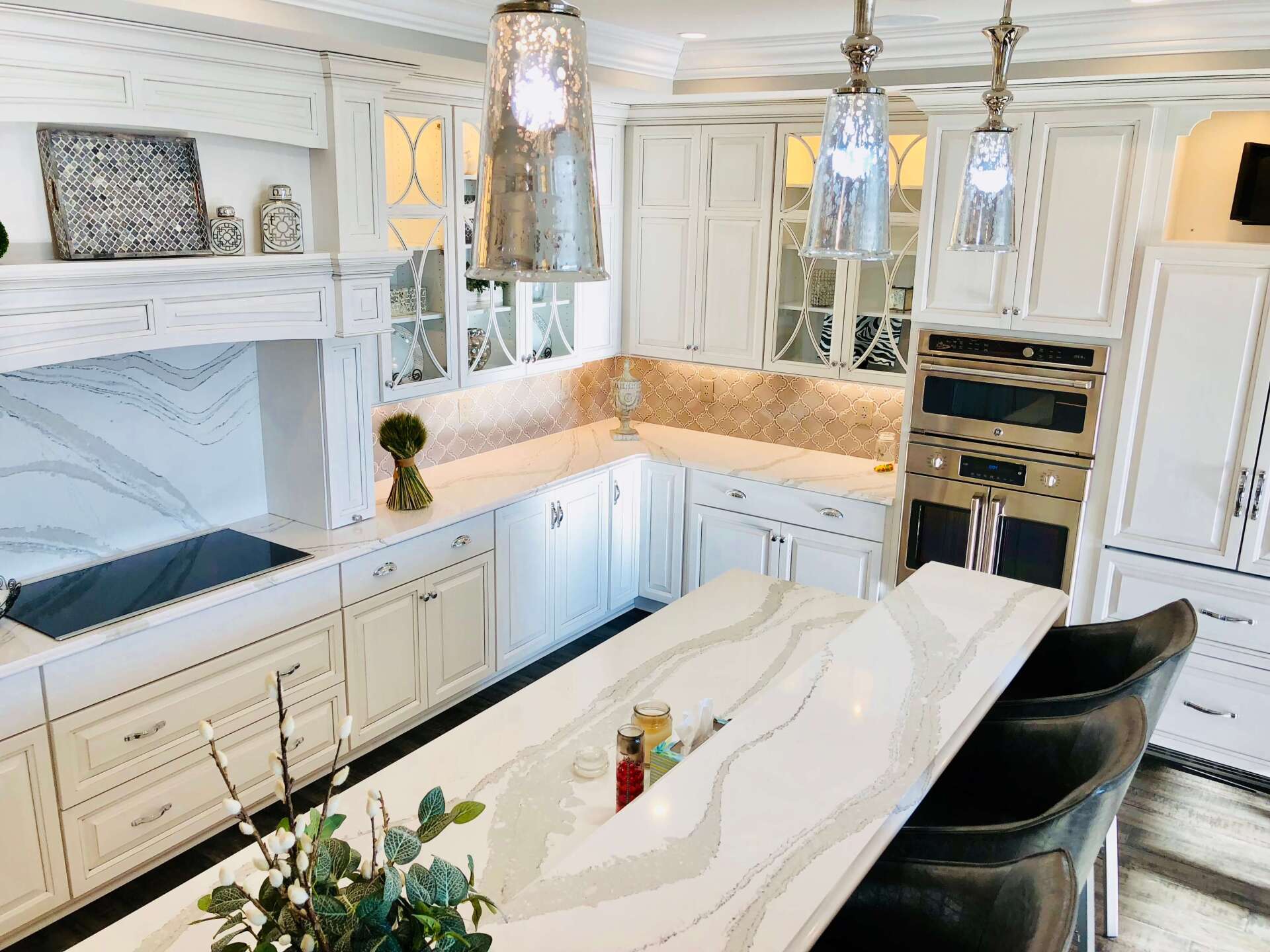 Bright white kitchen with marble countertops, built-in cabinets, and pendant lights over a large island