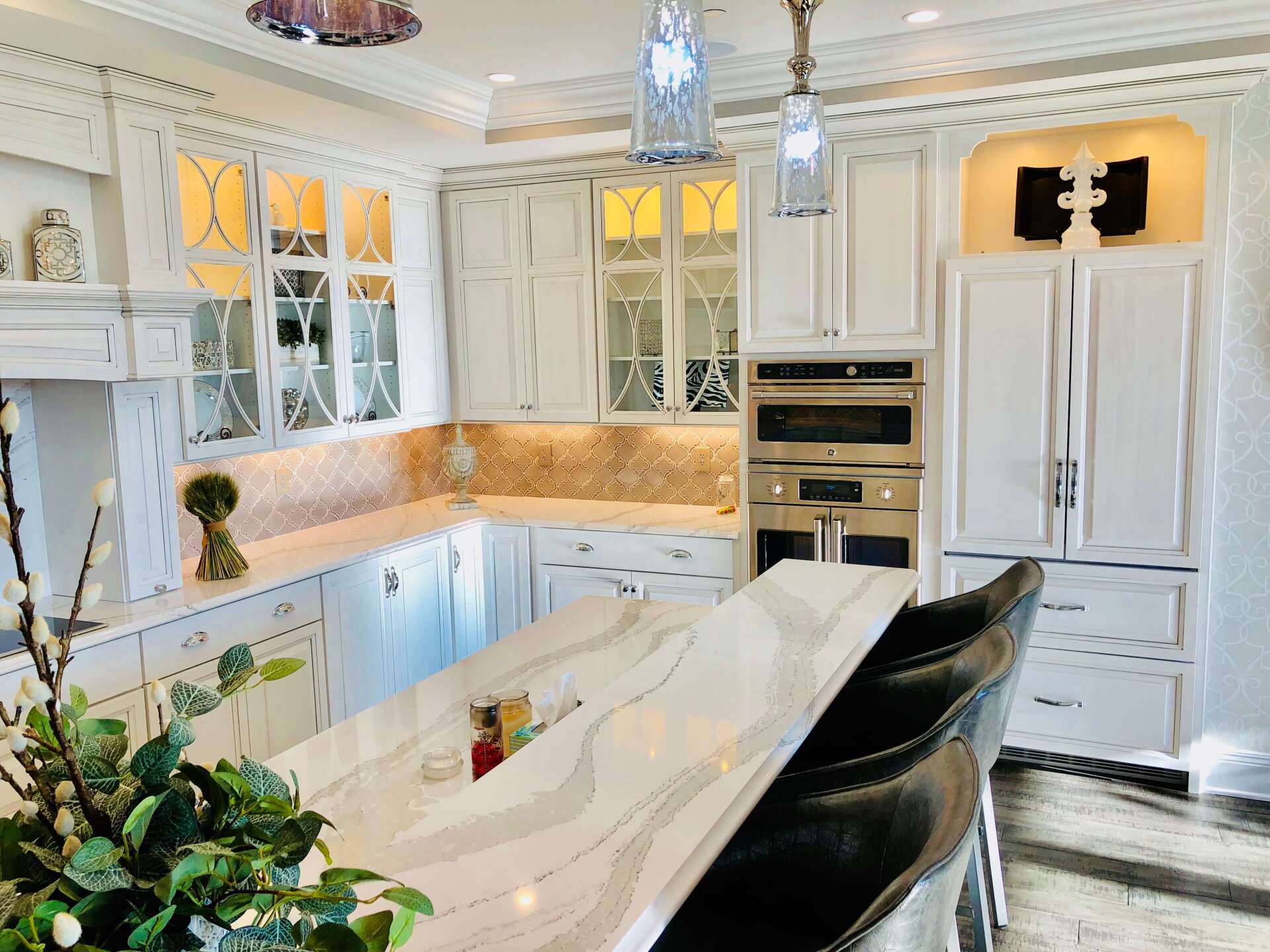 Bright white luxury kitchen with marble island, built-in appliances, glass cabinets, and warm under-cabinet lighting