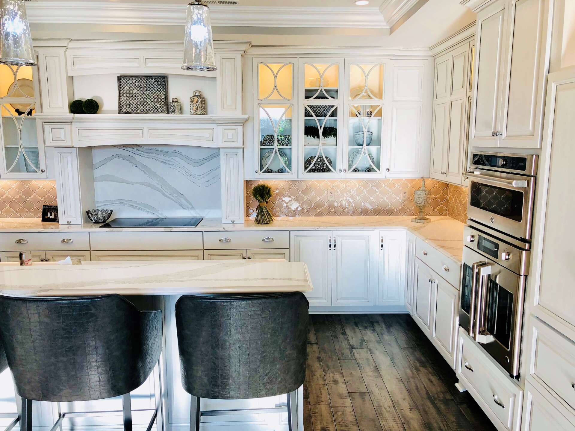Bright white kitchen with marble backsplash, black barstools, and built-in ovens.