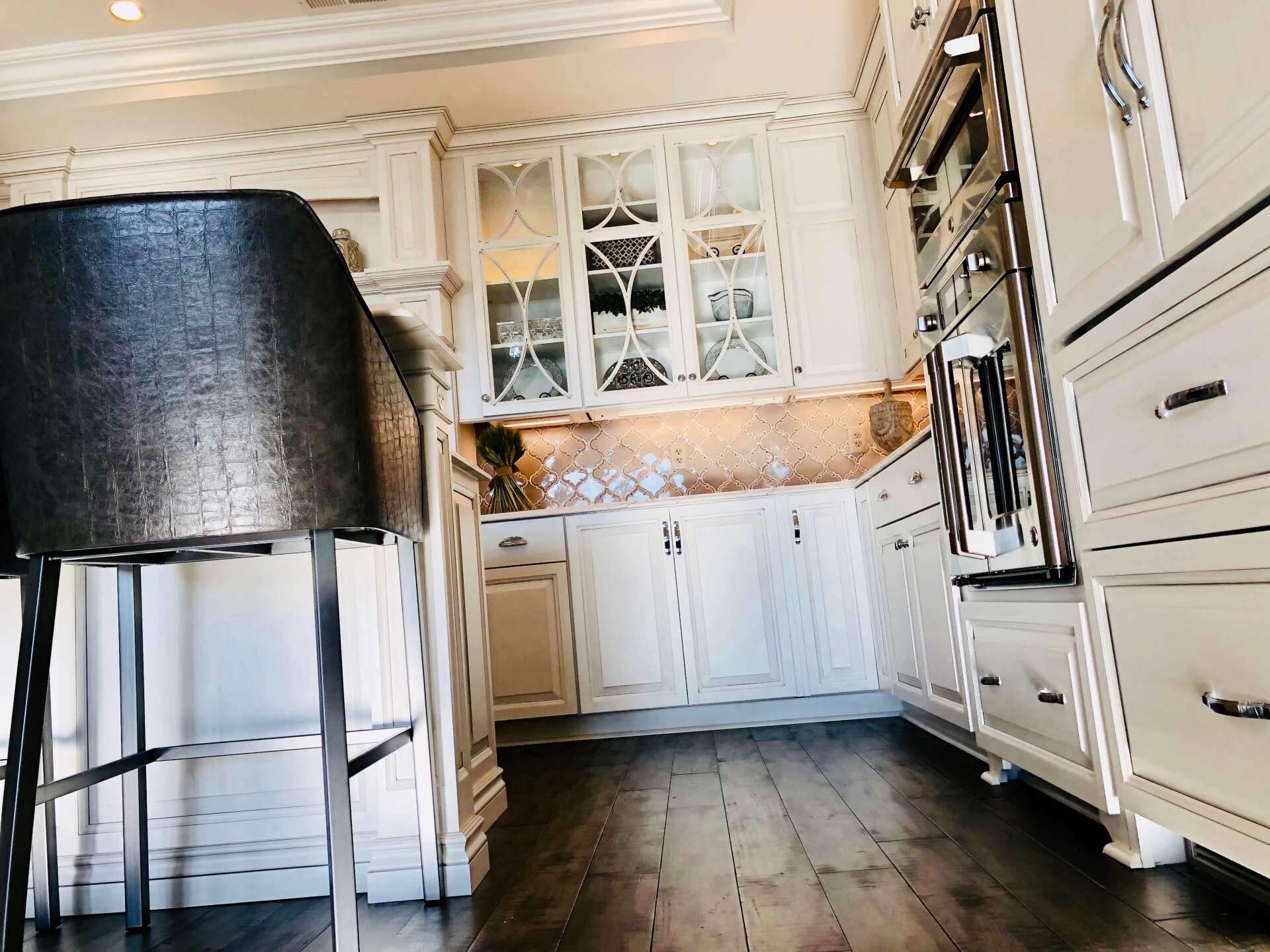 Bright kitchen with white cabinets, dark wood floor, and a large black island hood on the left.