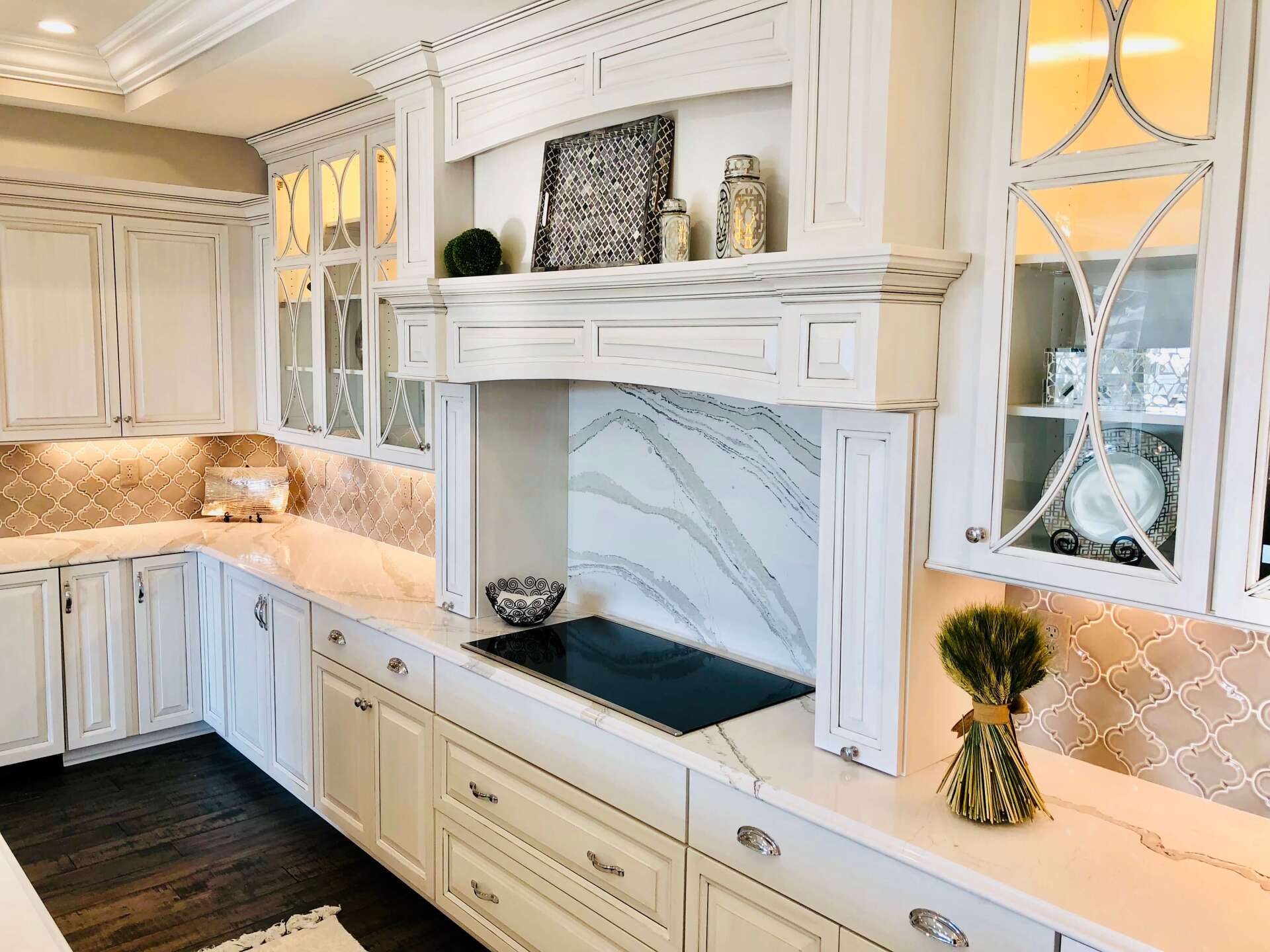 Bright white kitchen with marble counters, tile backsplash, and ornate cabinetry surrounding a stainless cooktop