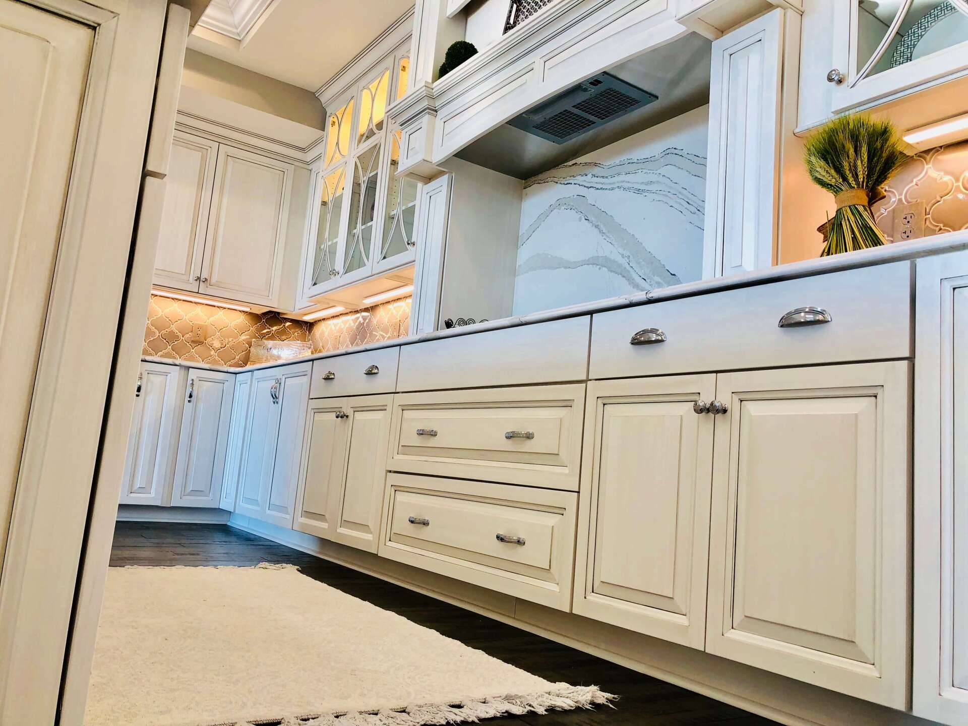 Bright white kitchen cabinets with marble countertops and a built-in cooktop, viewed from a low angle.