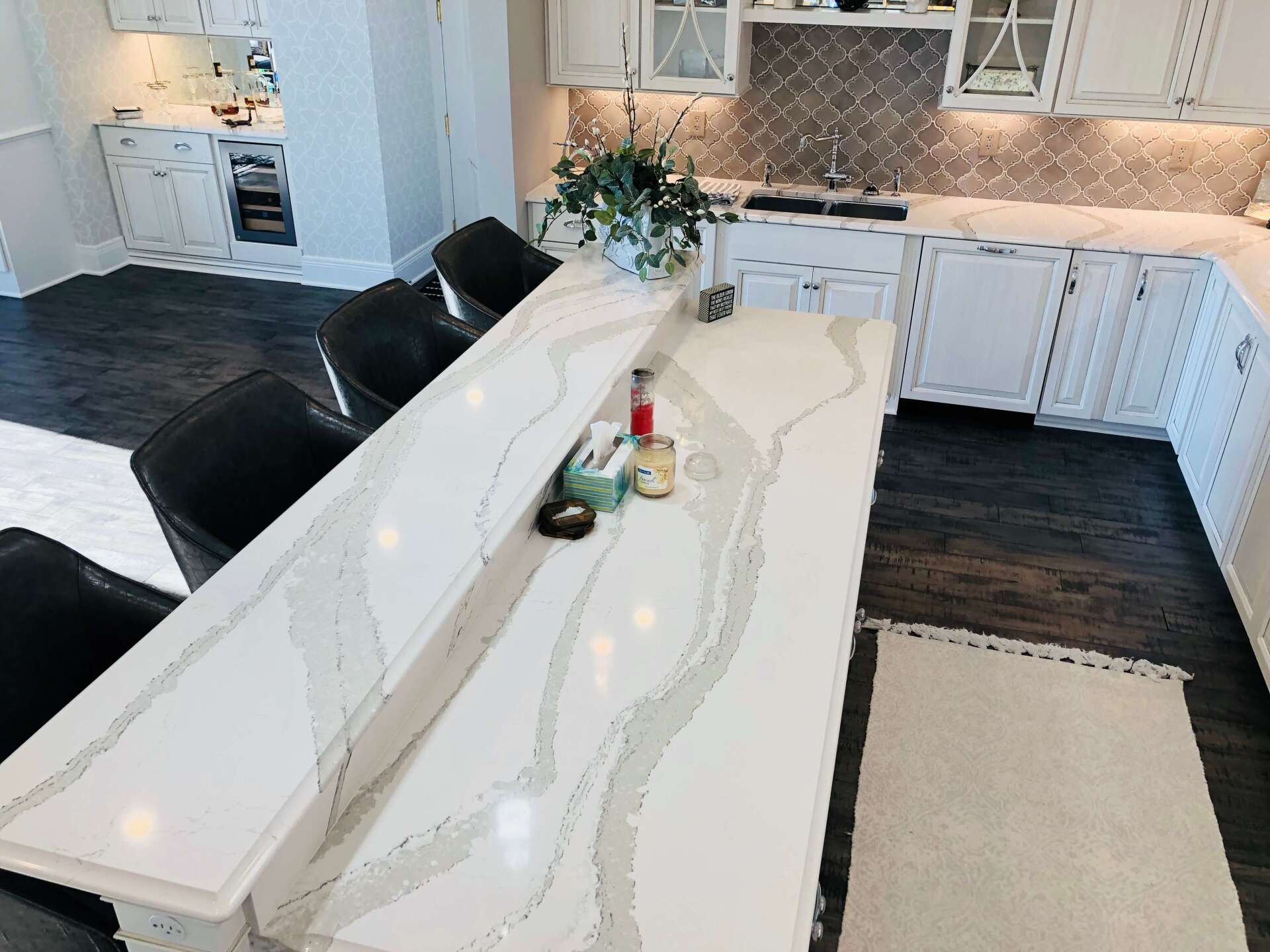 Modern kitchen with white island, black chairs, dark wood floors, and beige rug