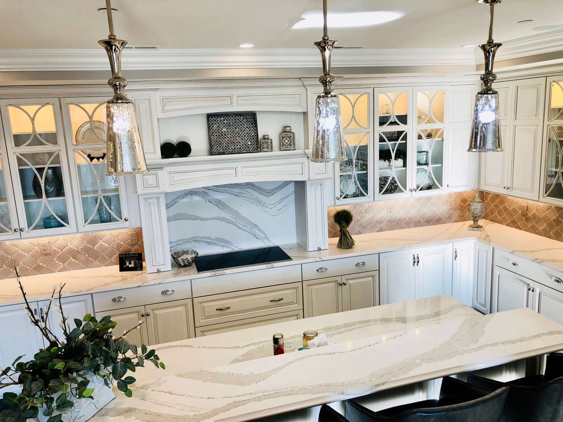Bright white kitchen with marble island, cabinets, and a large range hood under mirrored lights