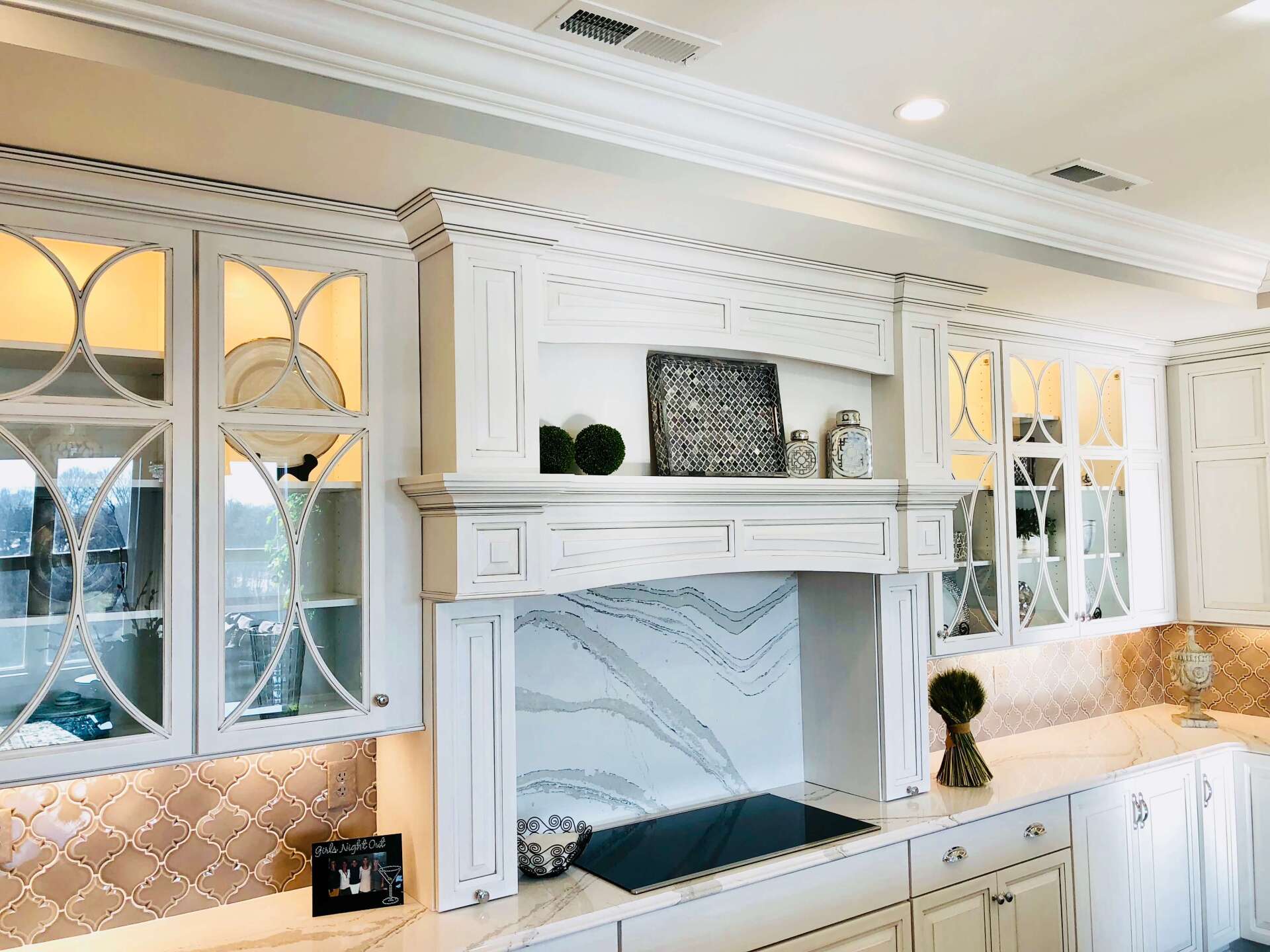 White kitchen with marble backsplash, built-in white cabinets, and a large arched window over the sink.