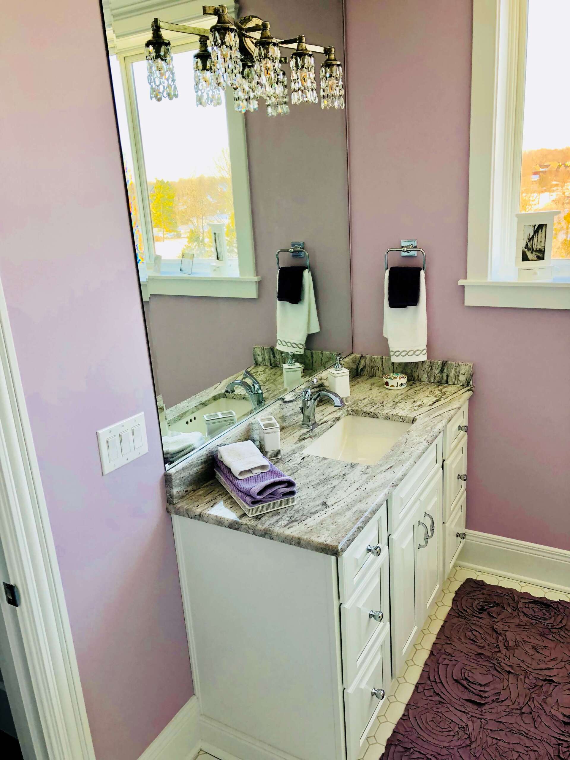 Bathroom vanity with marble countertop, mirror, and crystal chandelier in a pink-walled room